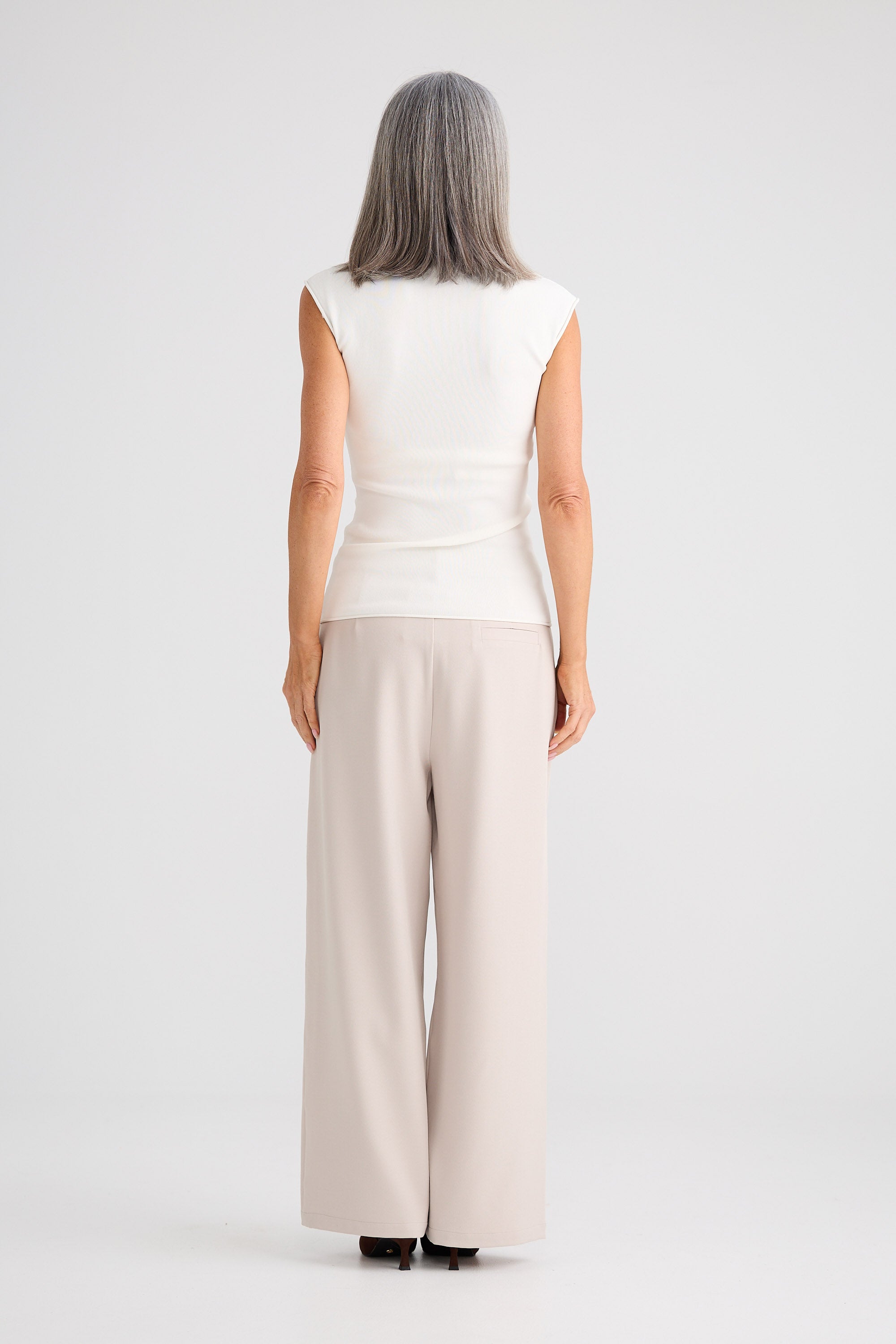 Woman wearing a white sleeveless top and beige wide-leg pants on a white background
