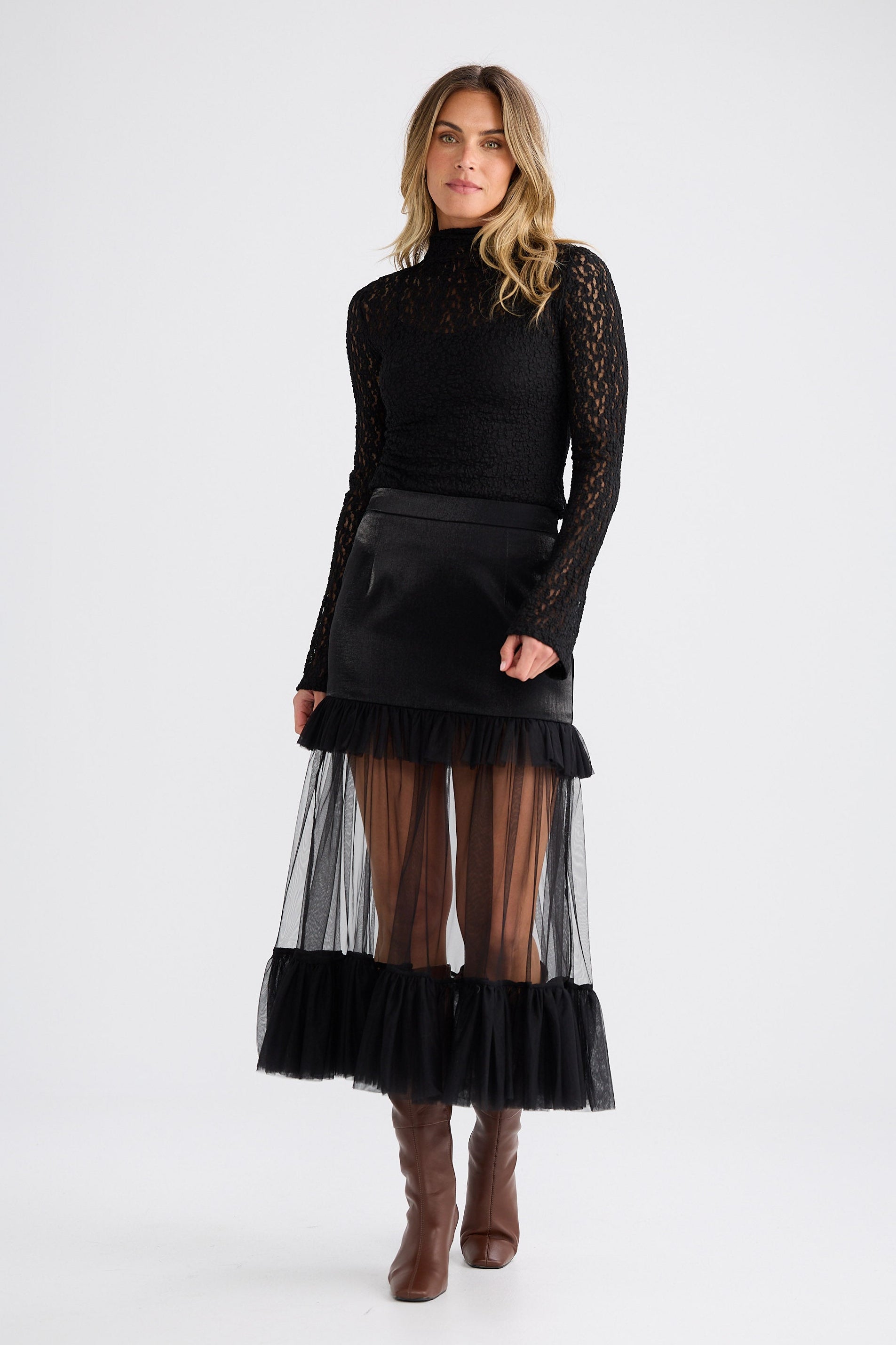 Woman wearing a black turtleneck with sheer sleeves and a black and sheer skirt on a white background