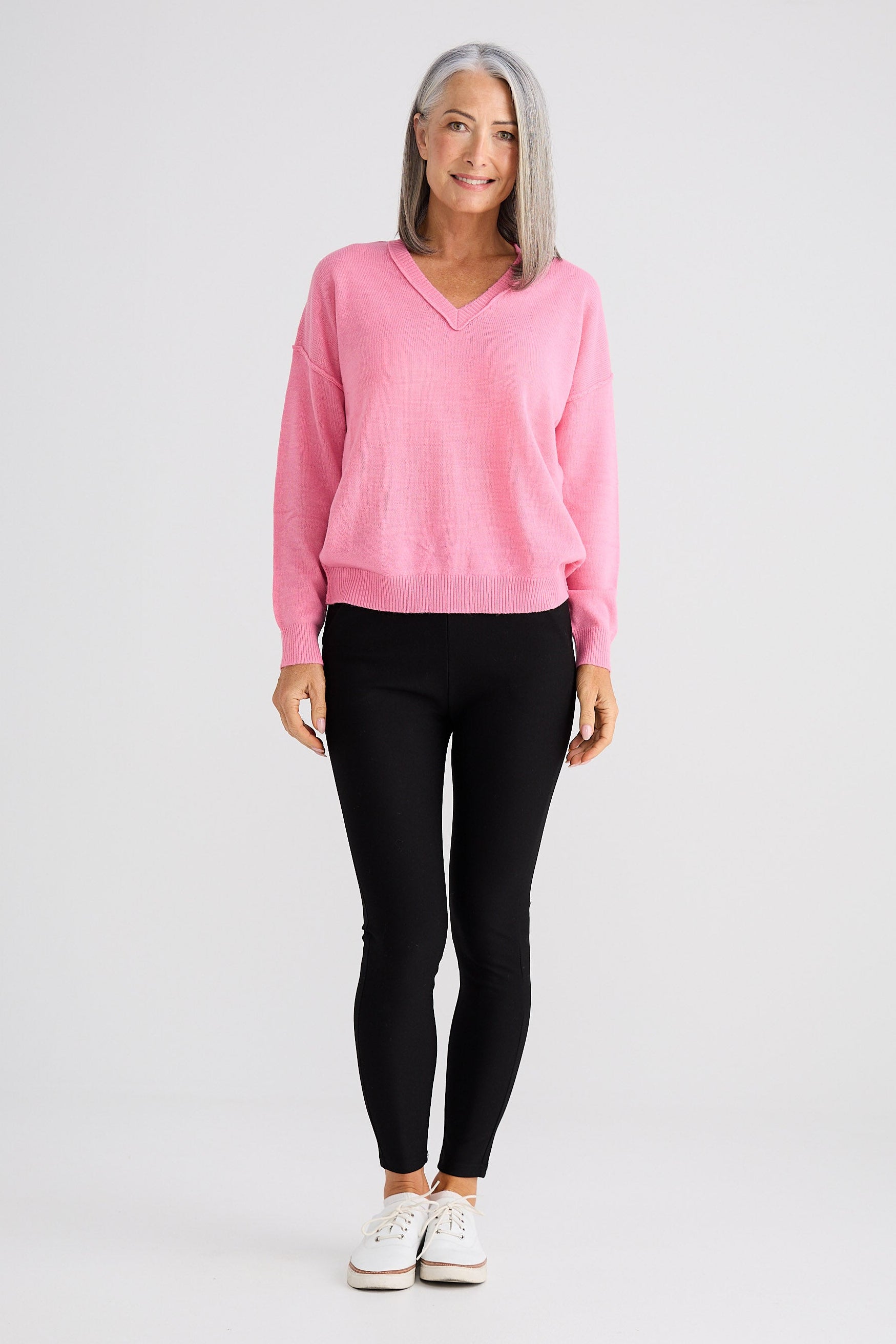 Woman wearing a pink sweater and black leggings on a white background
