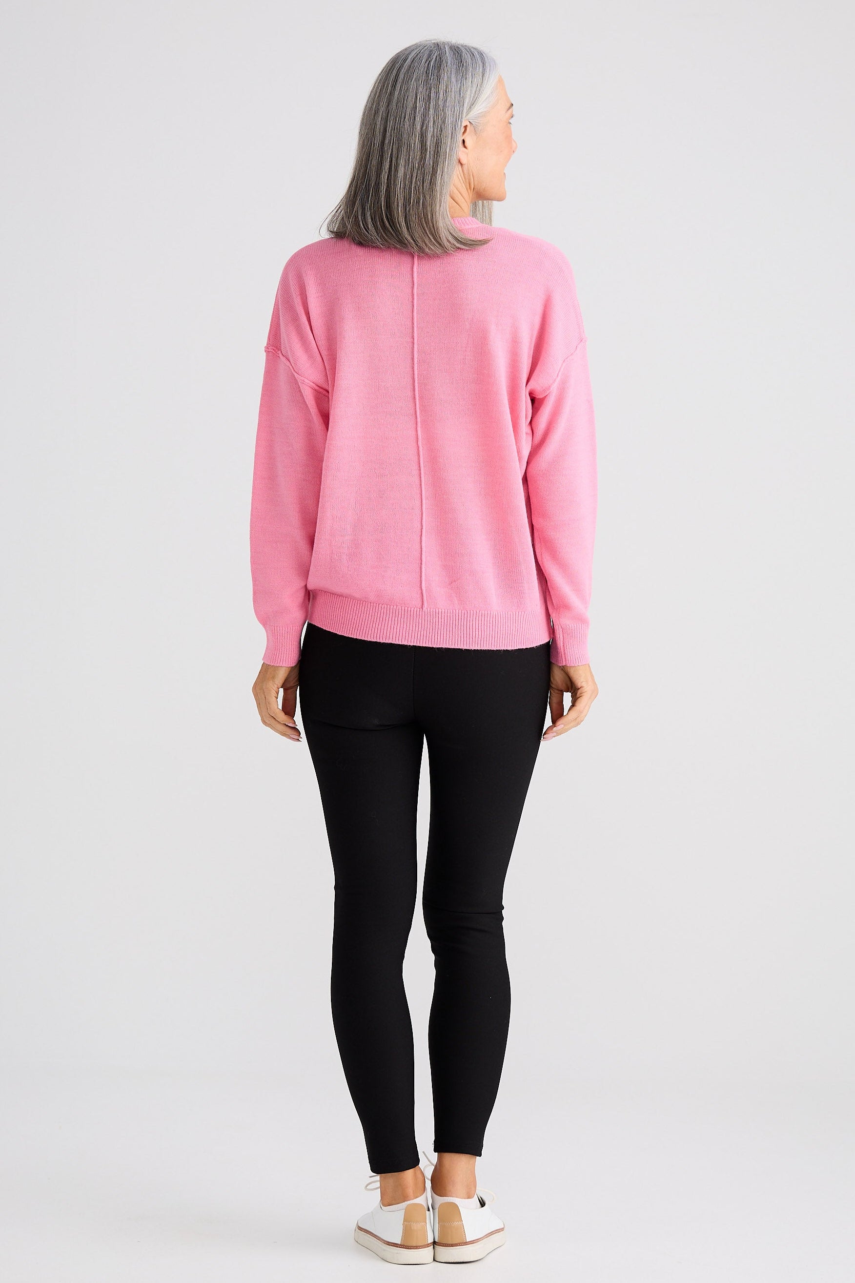 Person wearing a pink sweater and black leggings on a white background