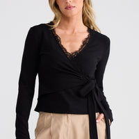Woman wearing a black top with lace details and beige pants on a white background