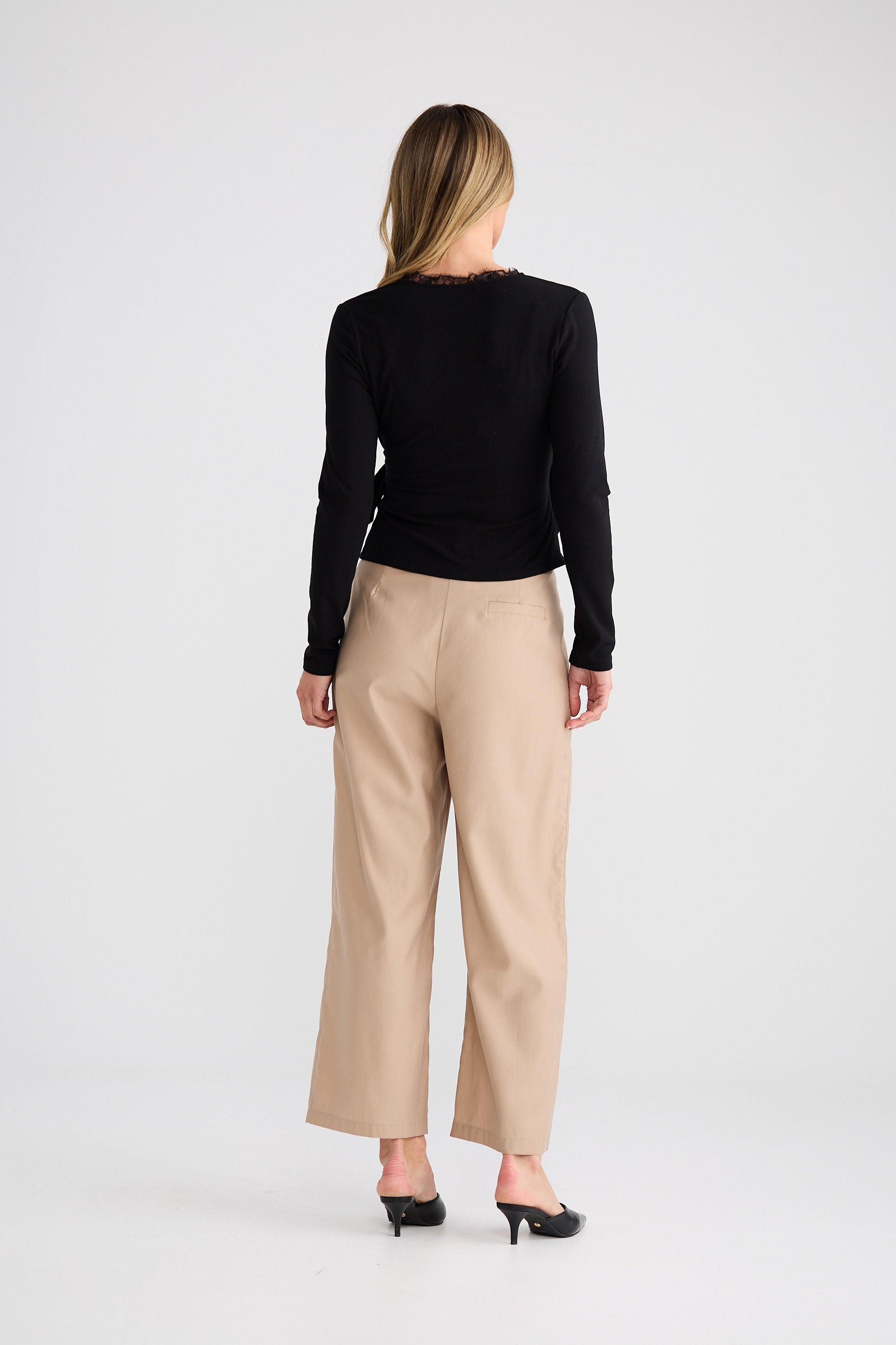 Woman wearing a black long-sleeve top and beige pants on a white background