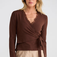 Woman wearing a brown wrap top with beige pants on a white background