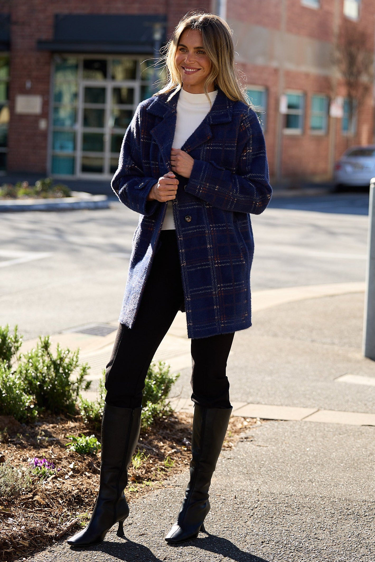 Woman in a plaid coat standing on a sidewalk with a city street background