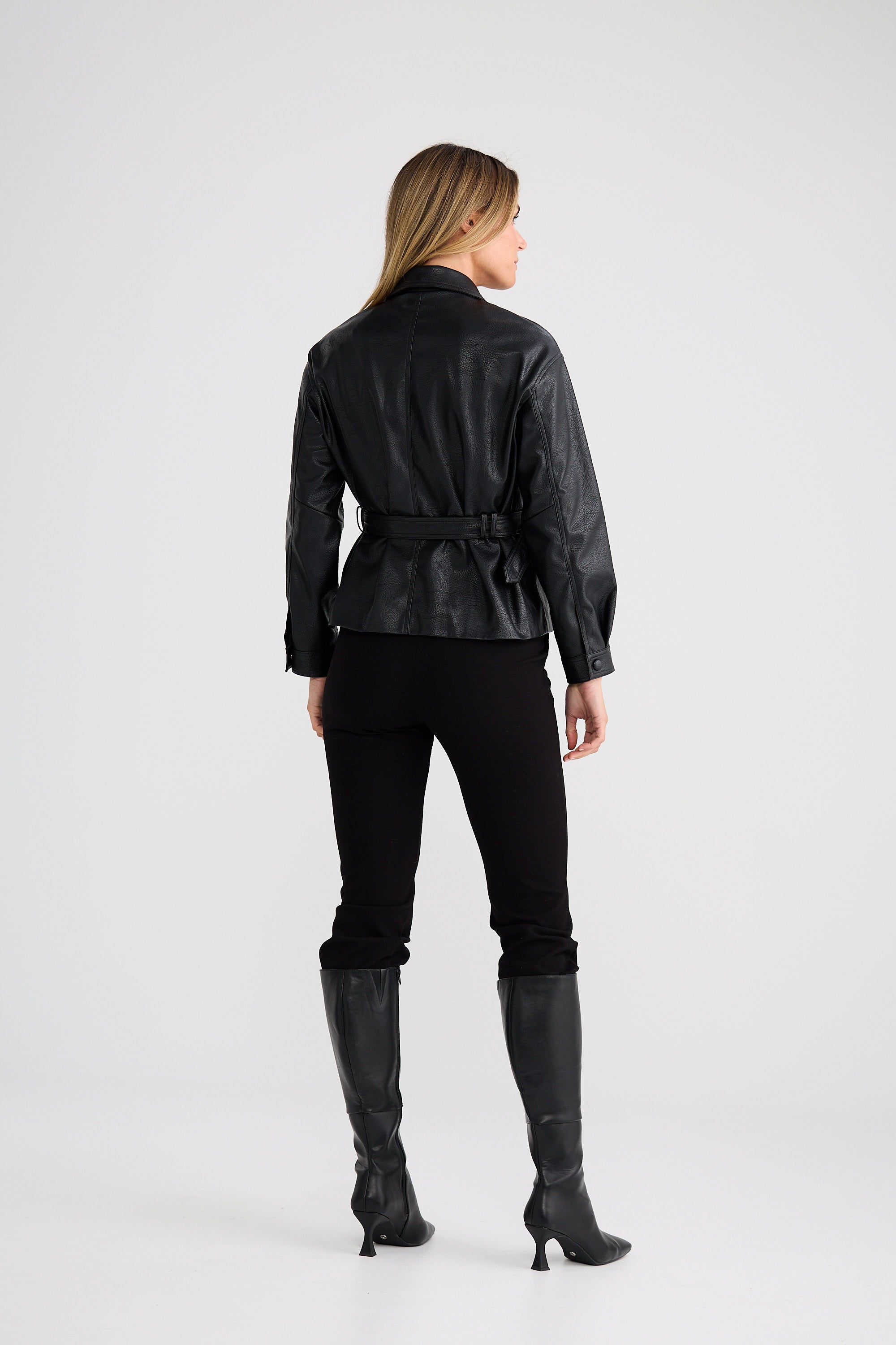 Woman wearing a black leather jacket and pants with gray boots on a white background
