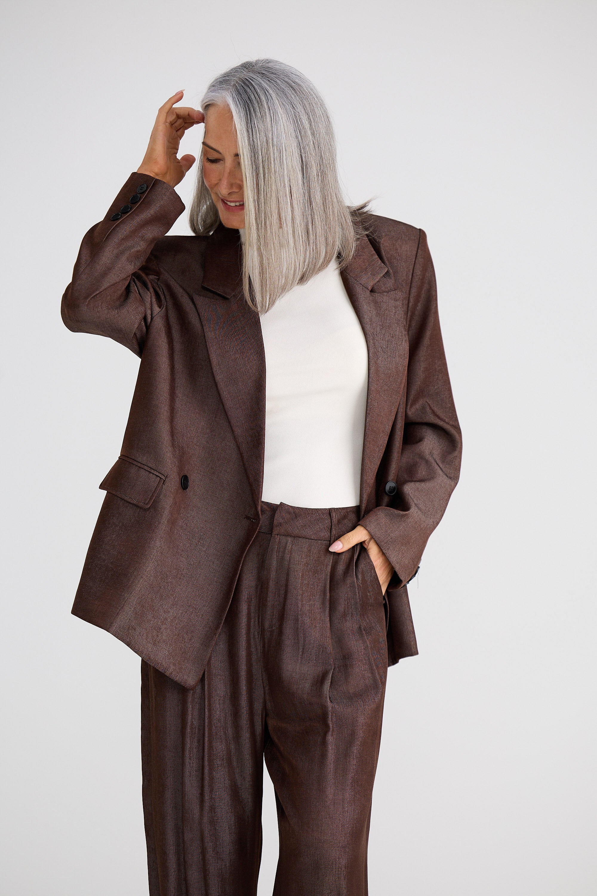 Woman wearing a brown suit with a white top against a plain background