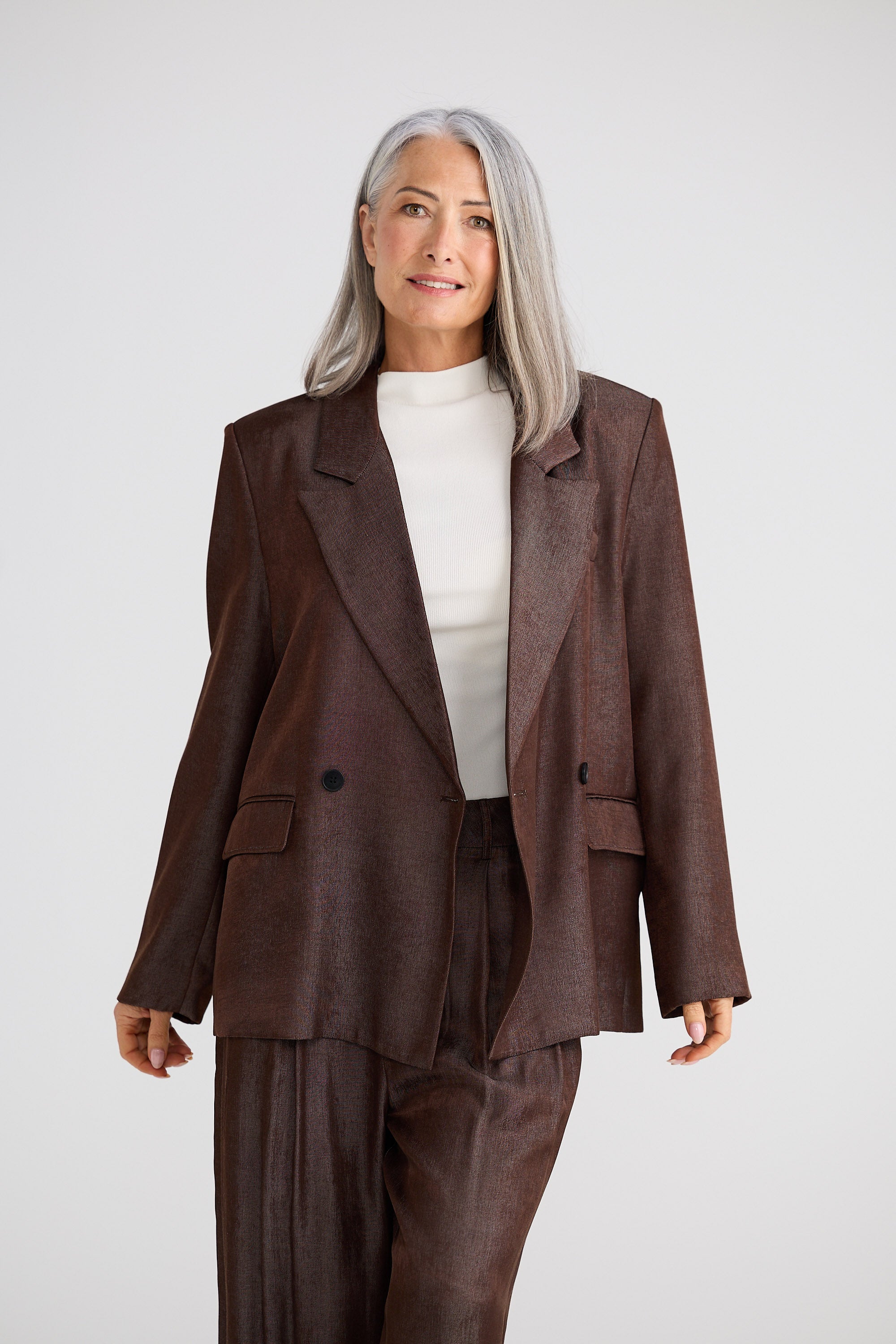 Woman wearing a brown suit with a white shirt on a plain background