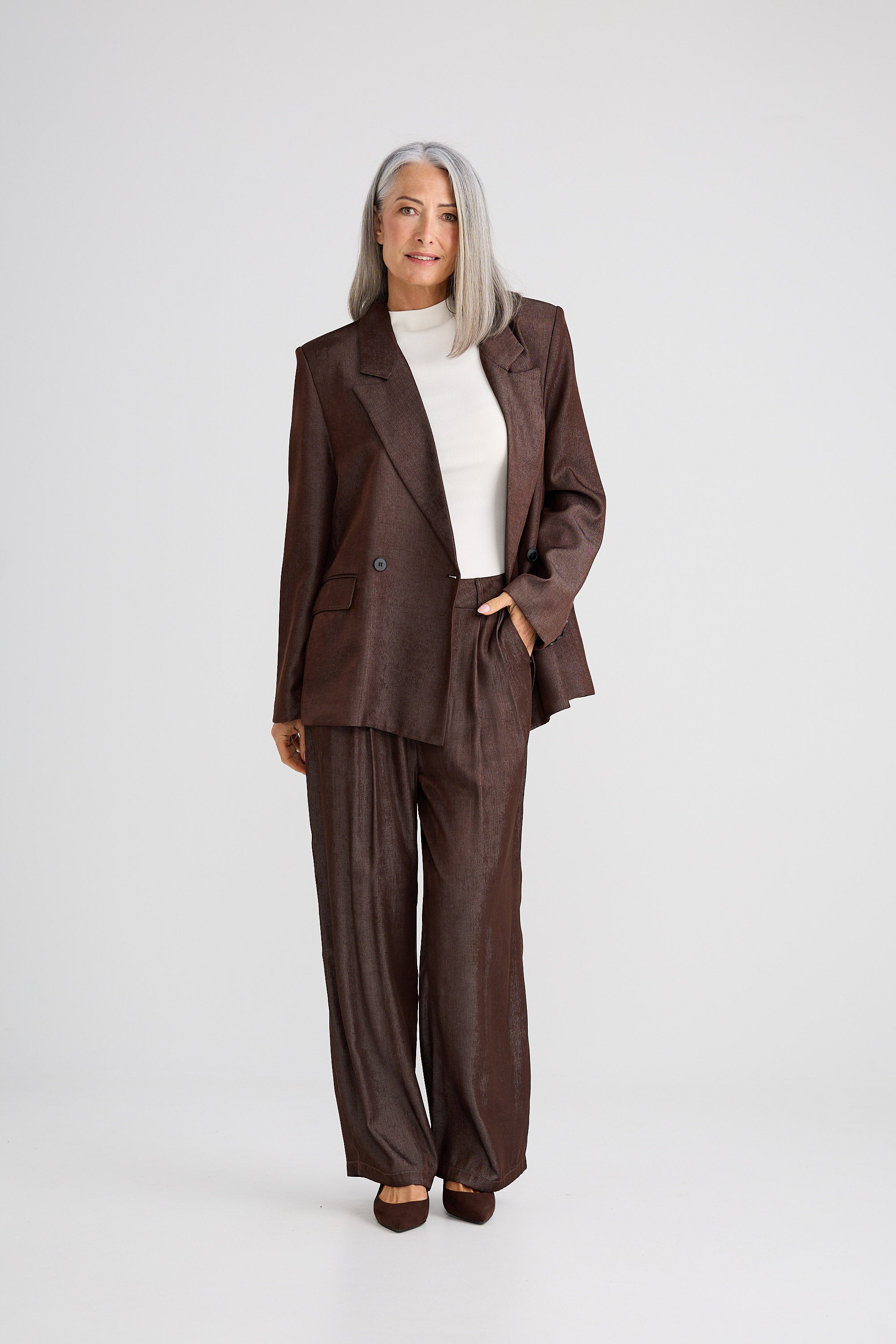Woman wearing a brown suit with a white top on a light gray background