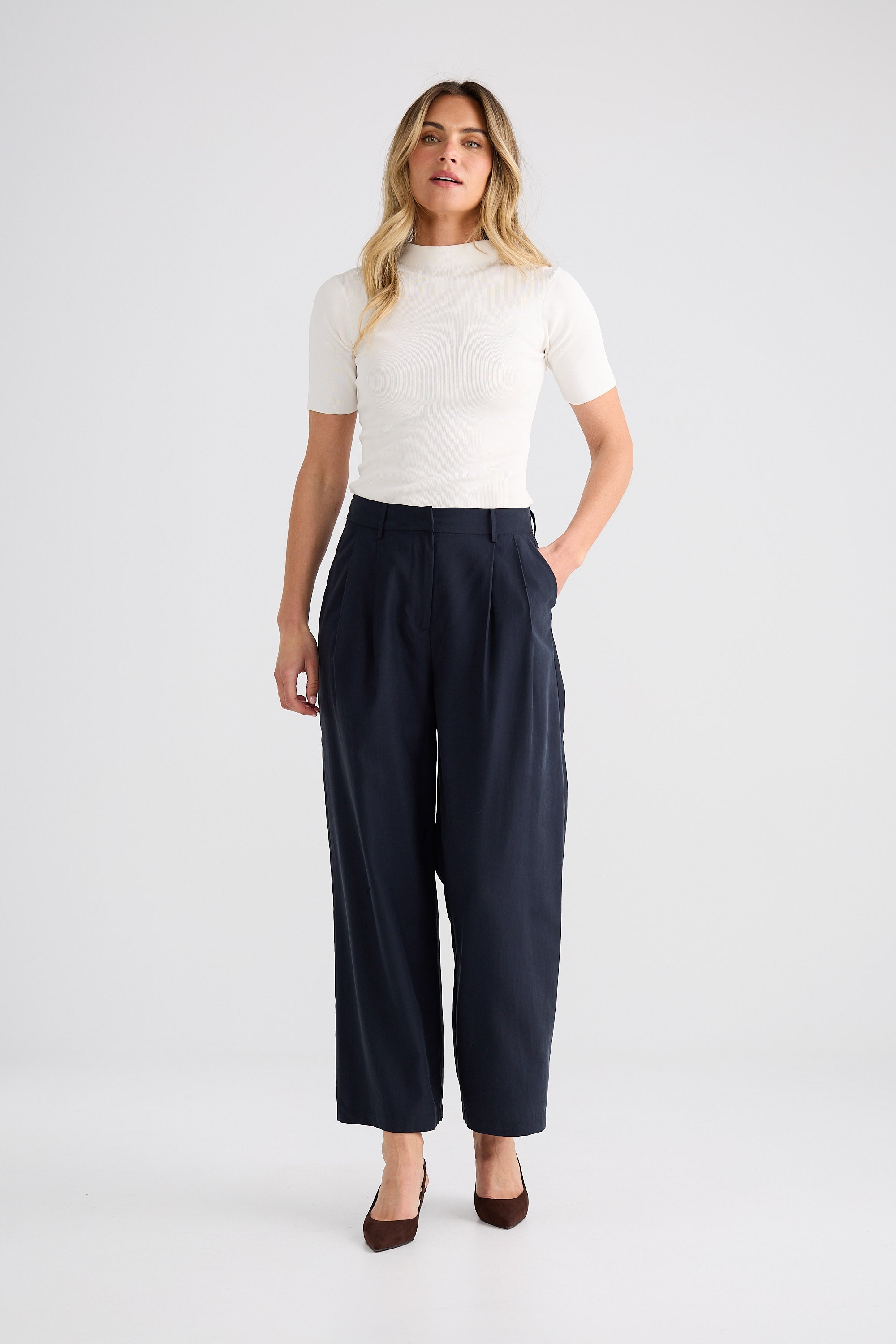 Woman wearing a white top and navy pants on a white background