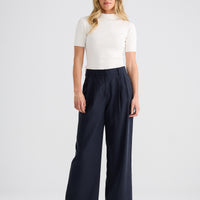 Woman wearing a white top and navy pants on a white background