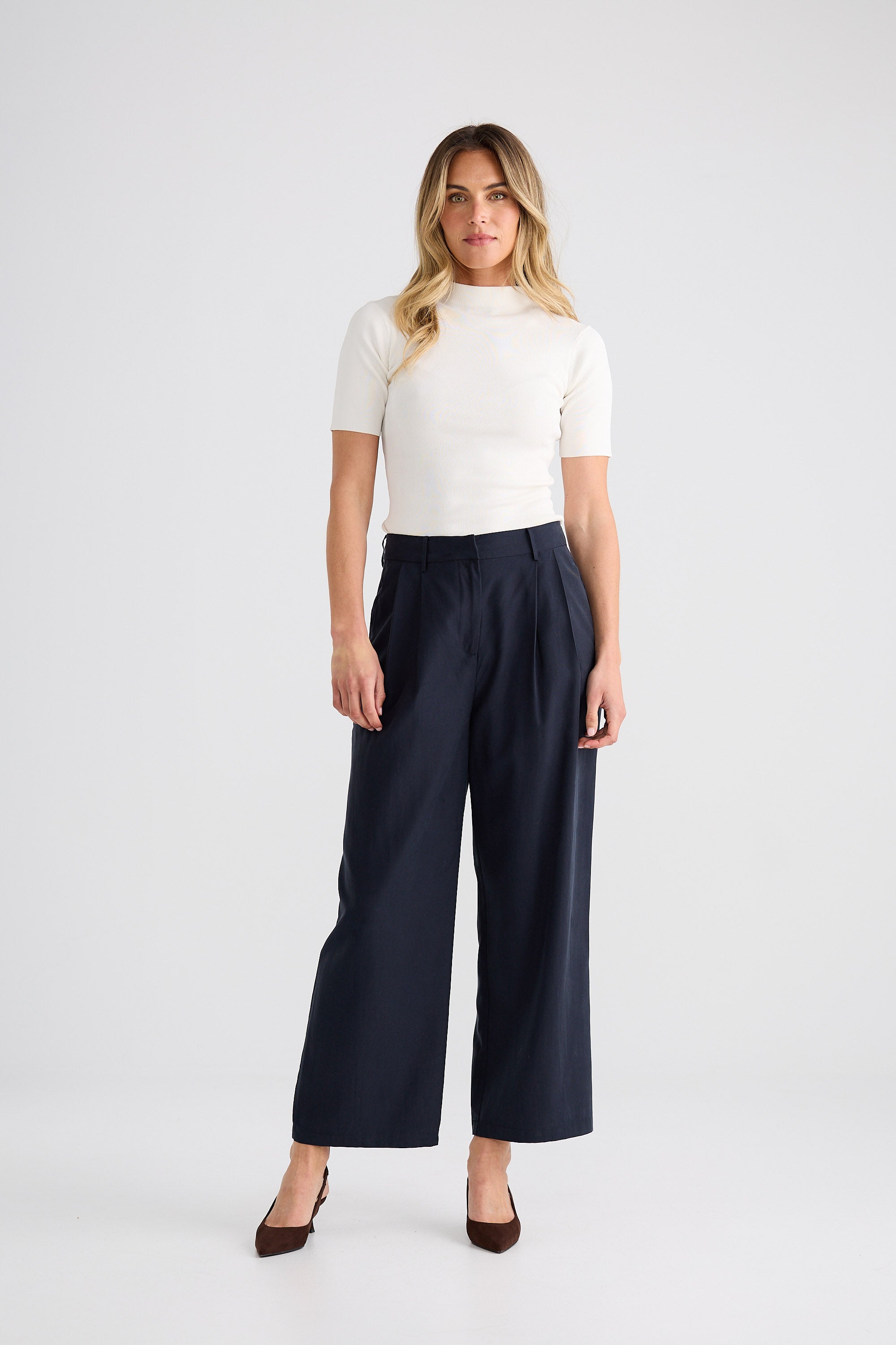 Woman wearing a white top and navy pants on a white background