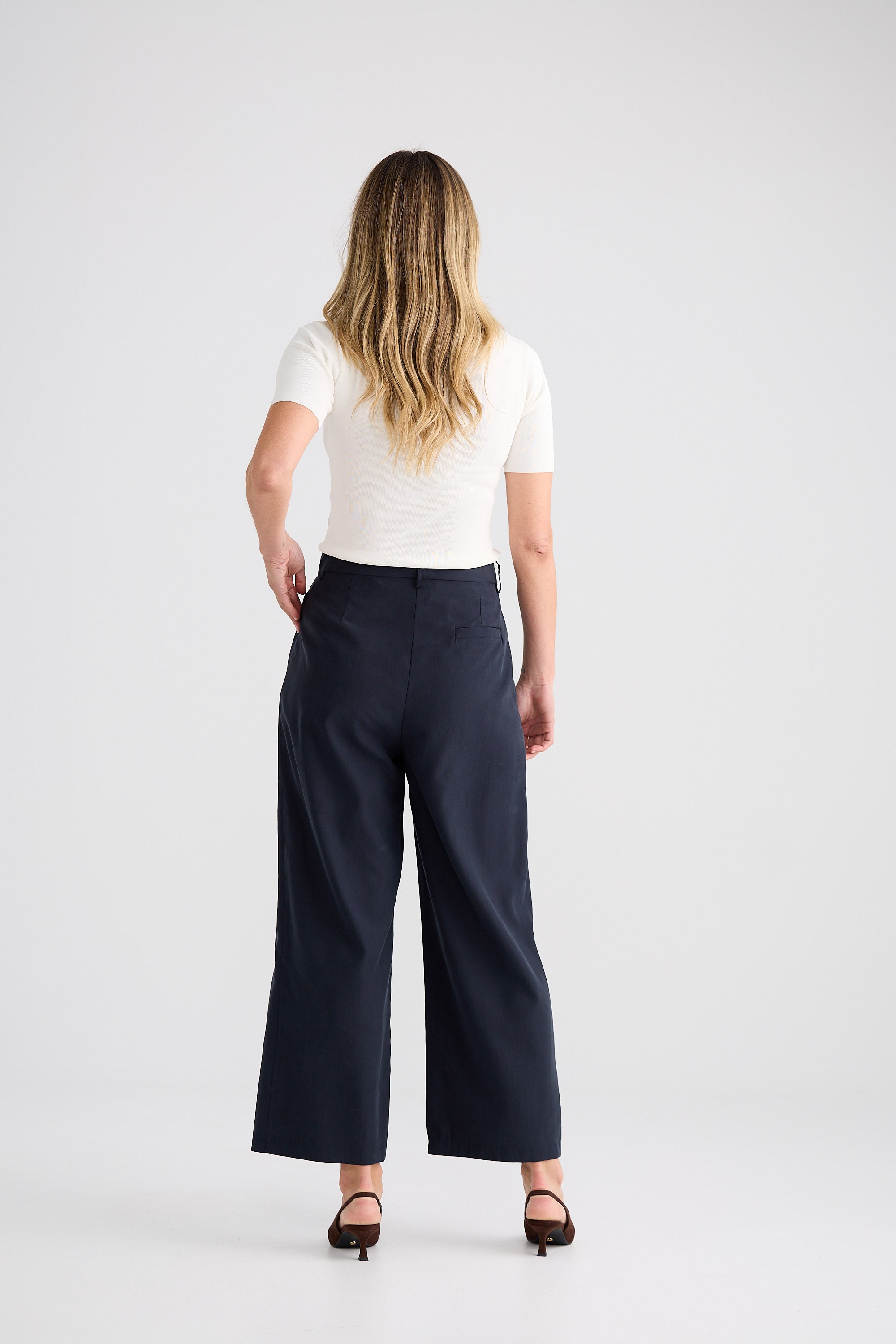 Person wearing navy wide-leg pants and a white top on a light gray background