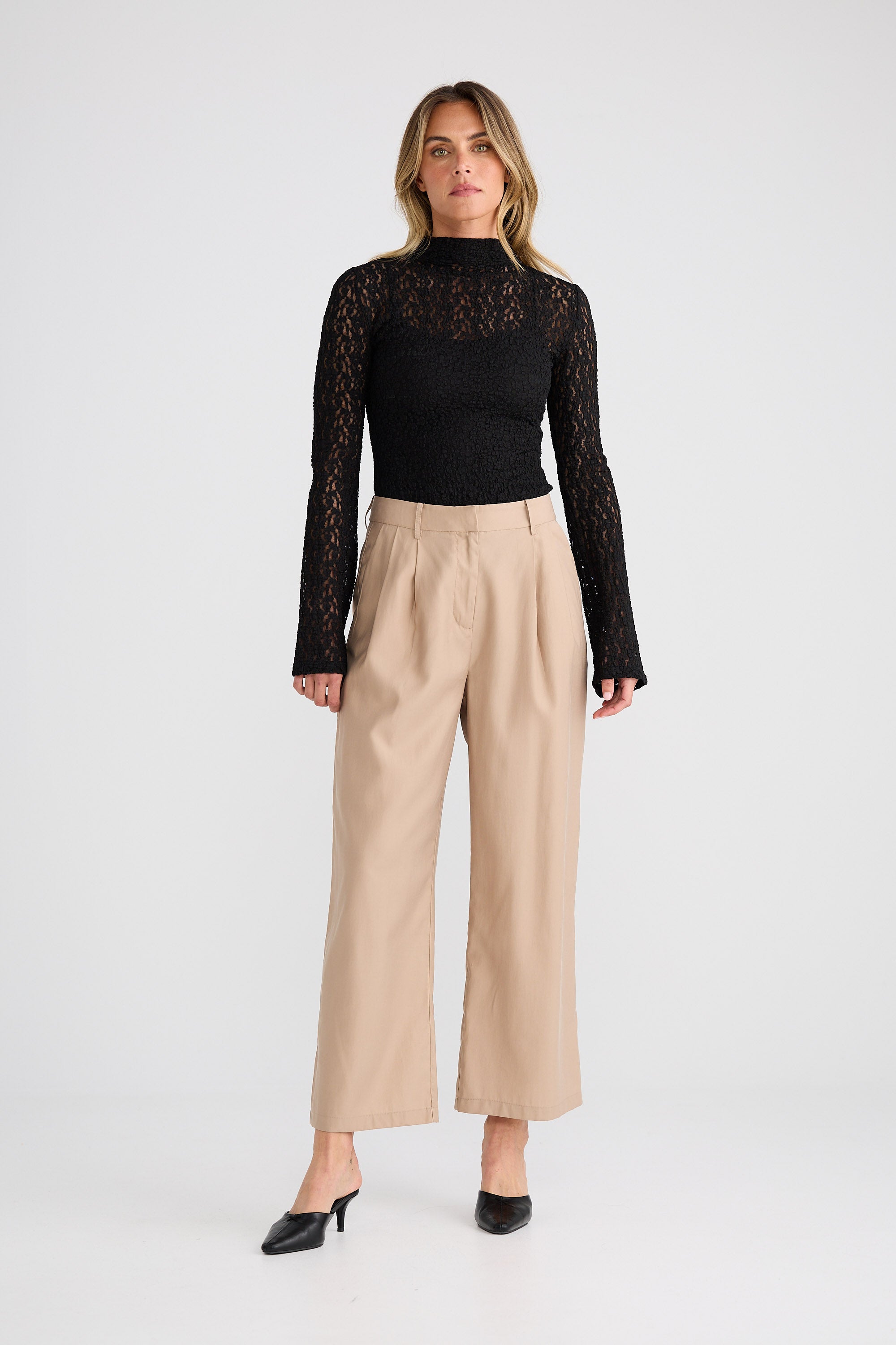 Woman wearing a black lace top and beige pants on a white background