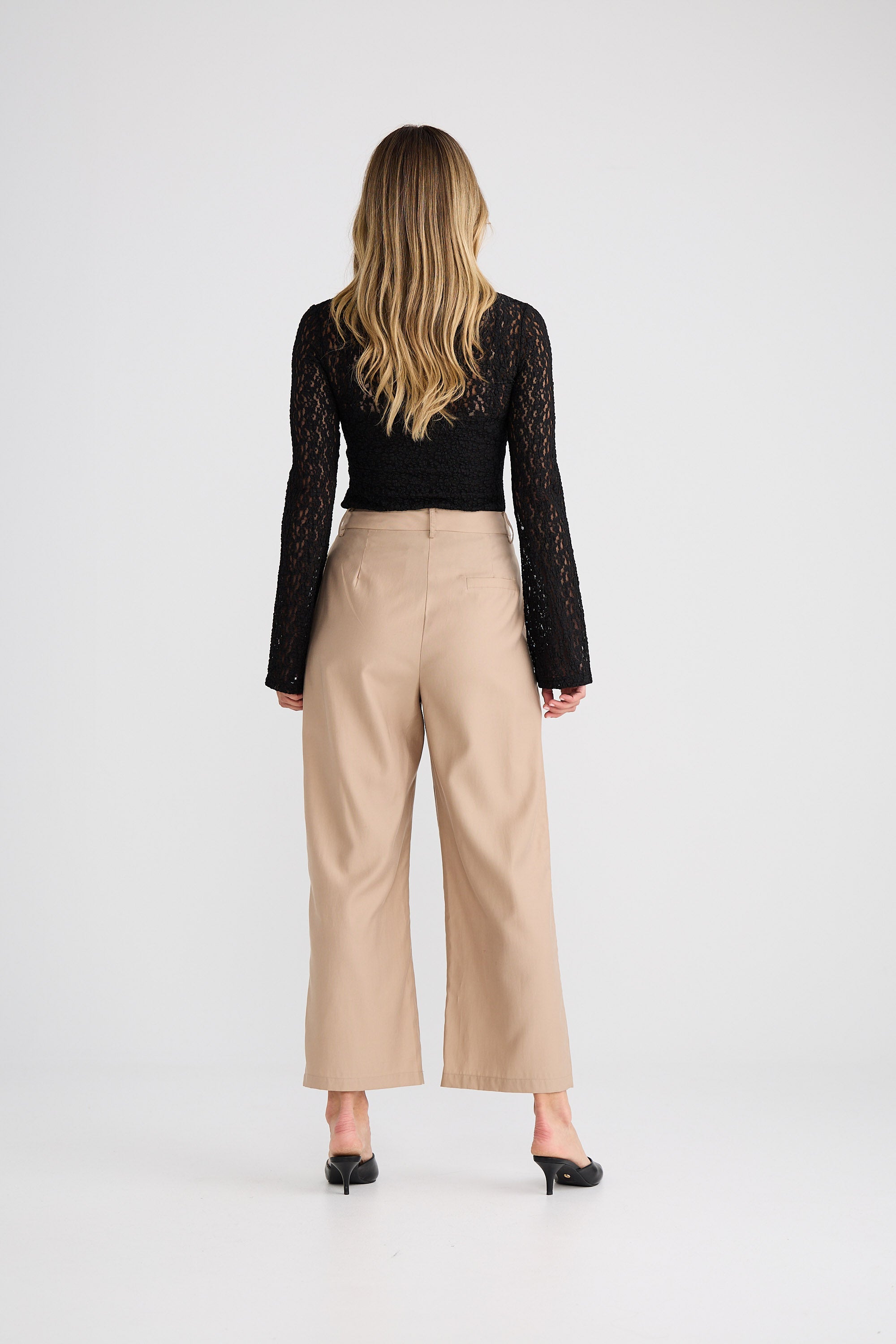 Person wearing a black lace top and beige pants on a white background