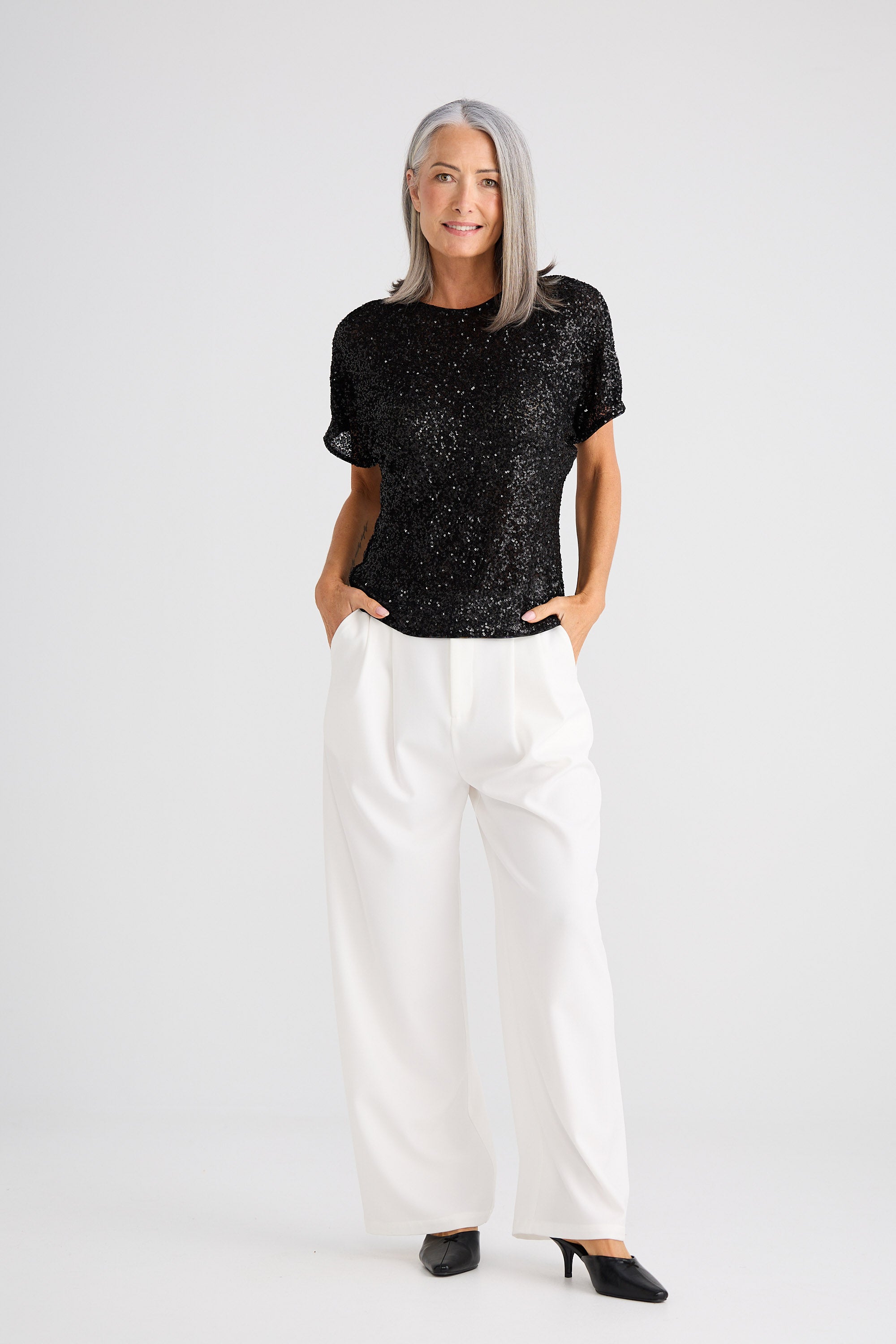 Woman wearing a black patterned top and white pants on a white background