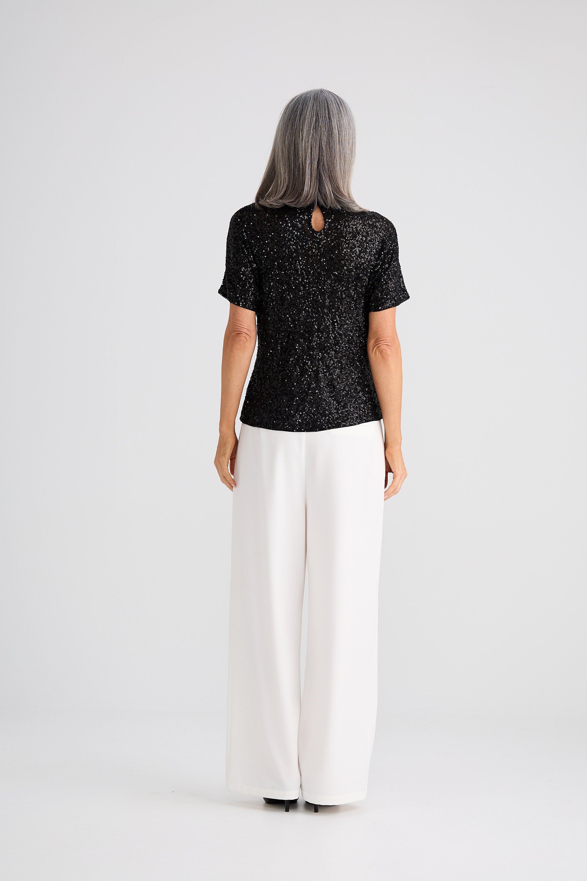 Person wearing a black patterned top and white pants on a white background