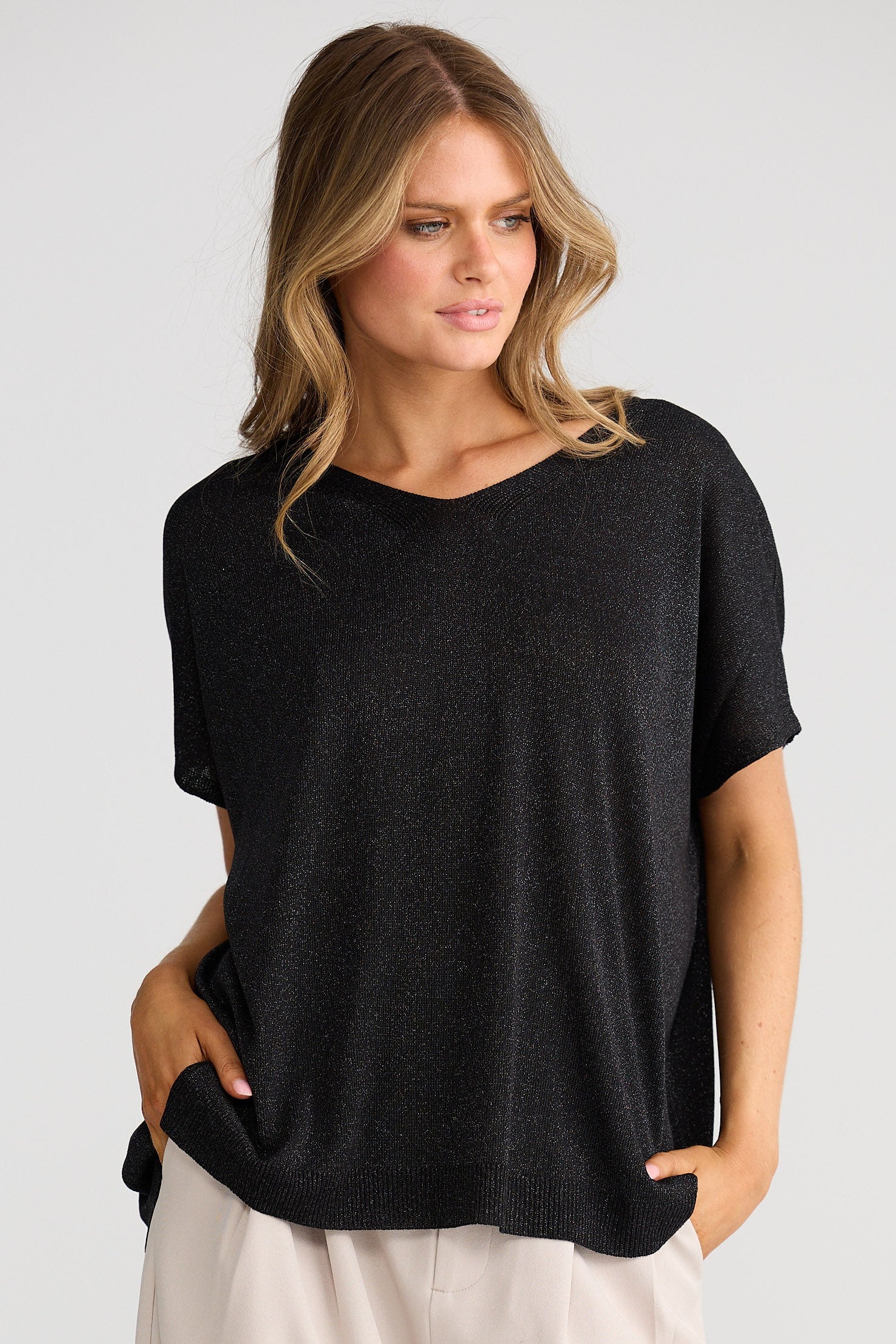 Woman wearing a black top and light-colored pants on a plain background