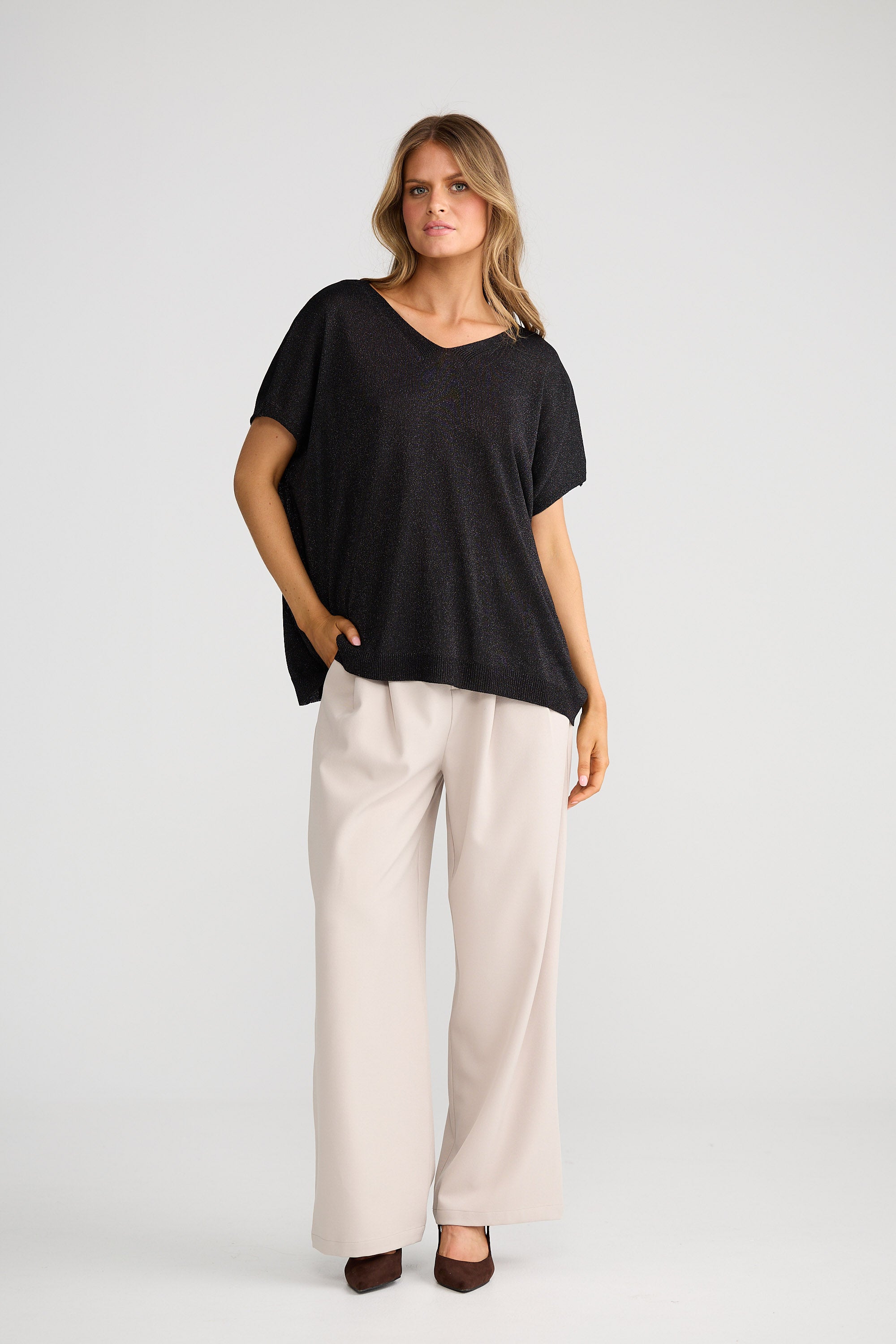 Woman wearing a black top and beige pants on a white background