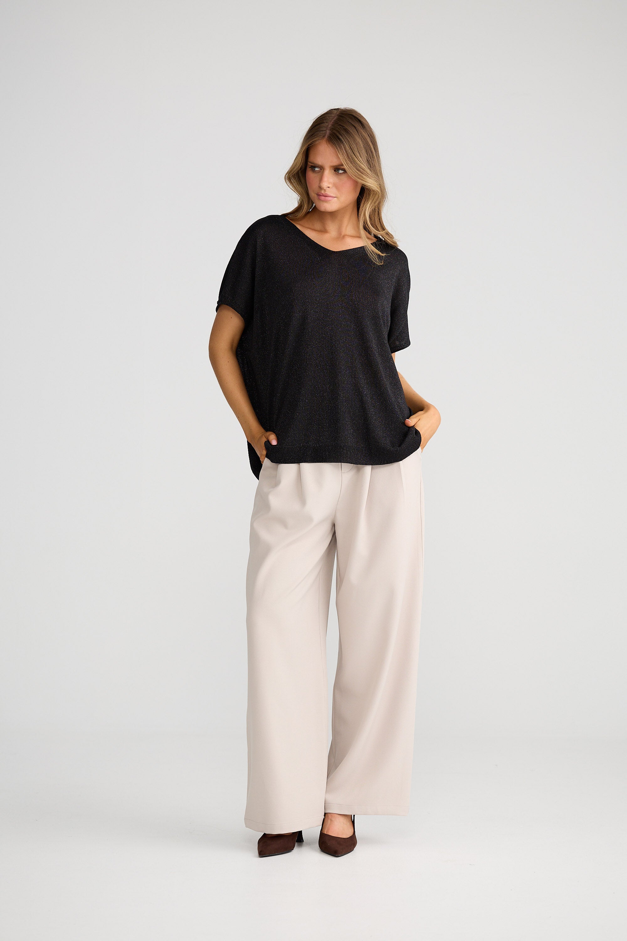 Woman wearing a black top and beige pants on a white background