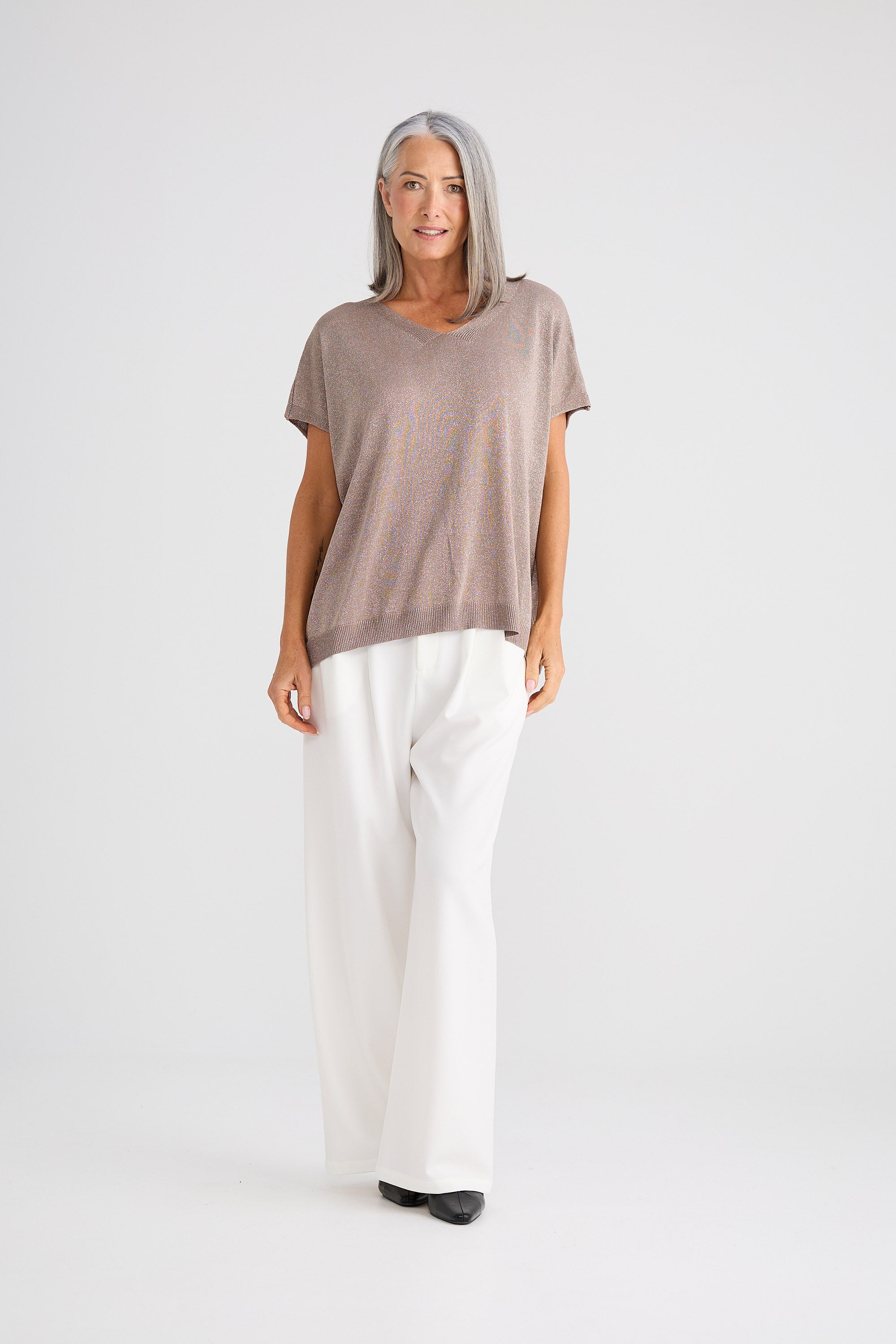 Woman wearing a brown top and white pants on a white background
