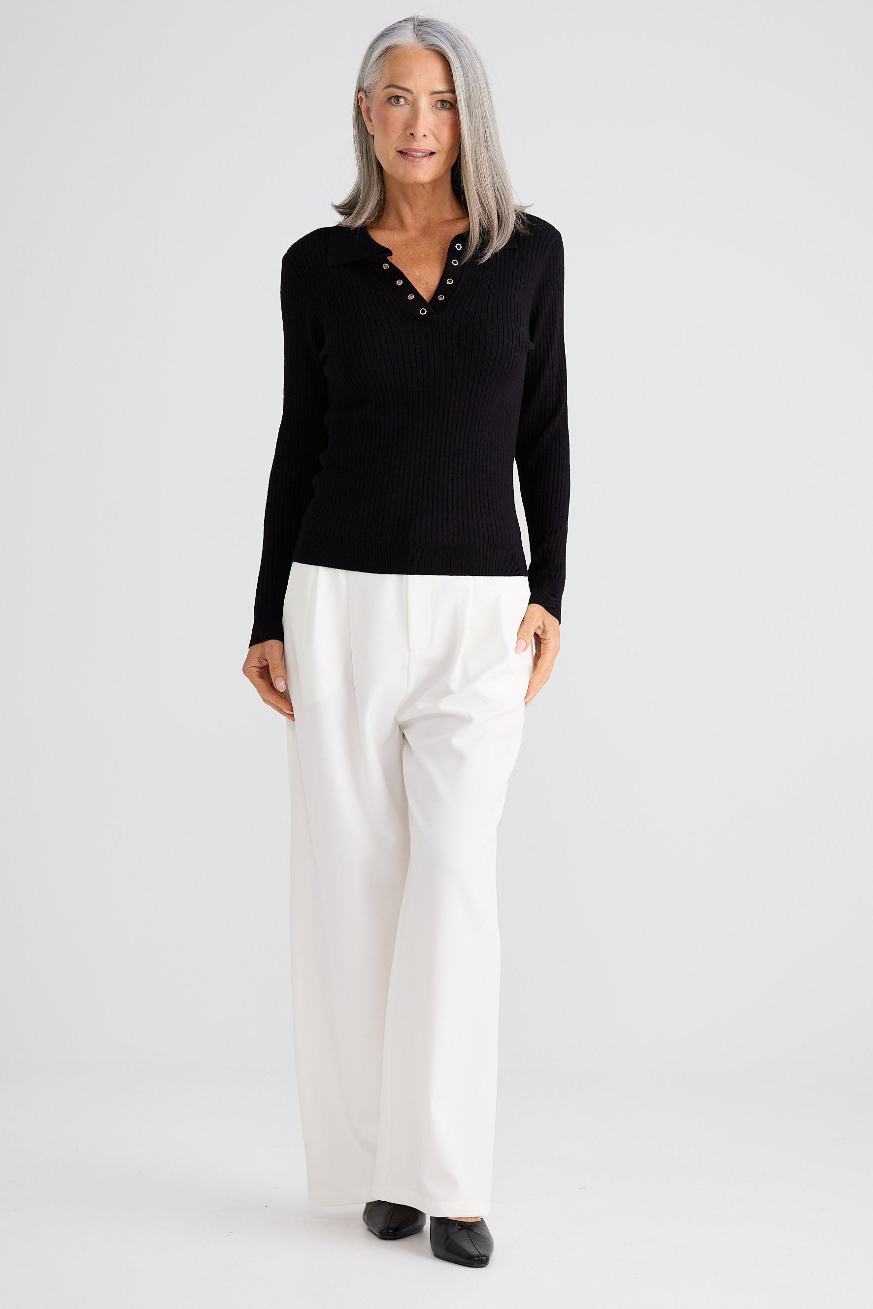 Woman wearing a black long-sleeve top and white pants on a white background