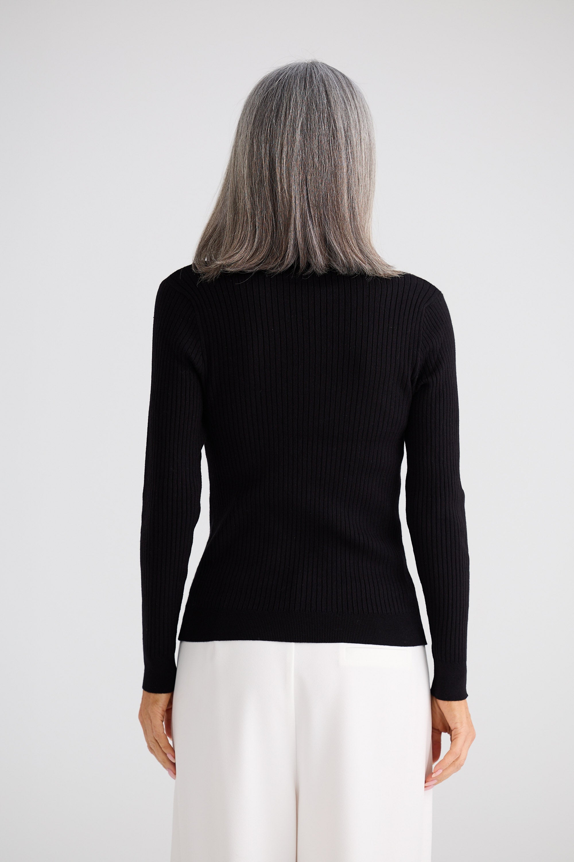 Person wearing a black ribbed long-sleeve top on a white background