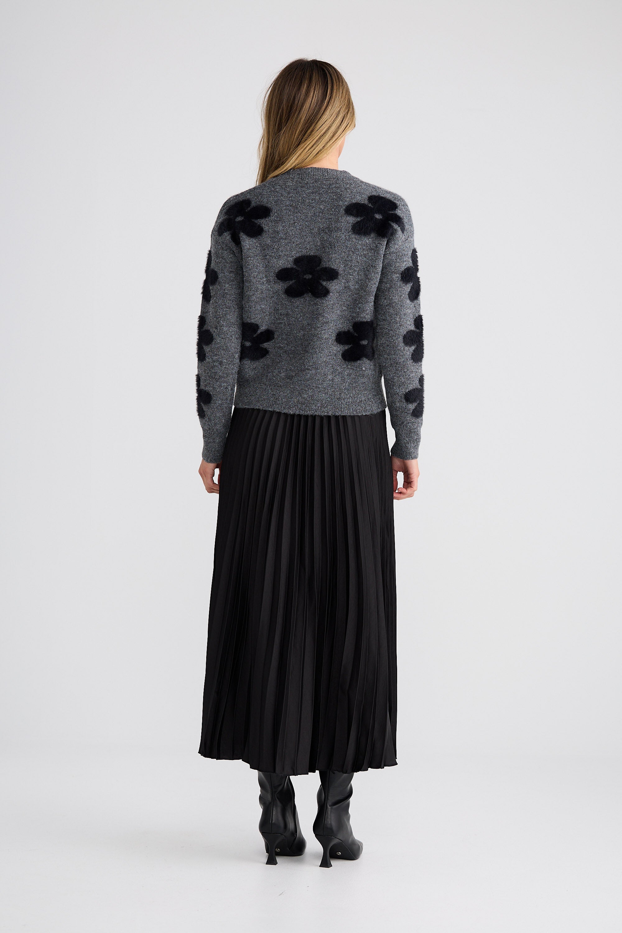 Woman wearing a gray sweater with black floral patterns and a long black skirt on a white background