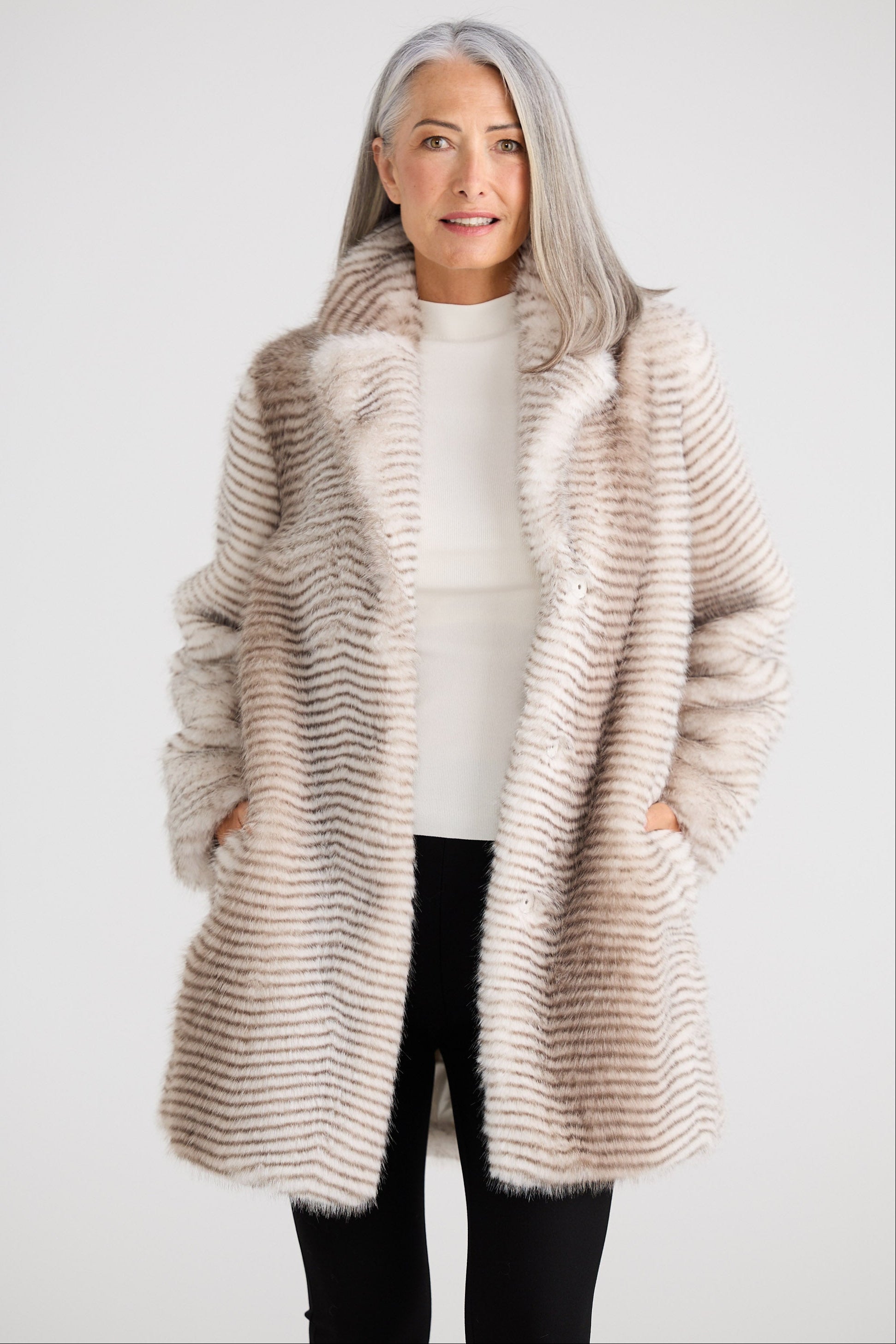 Woman wearing a long, light brown fur coat against a white background