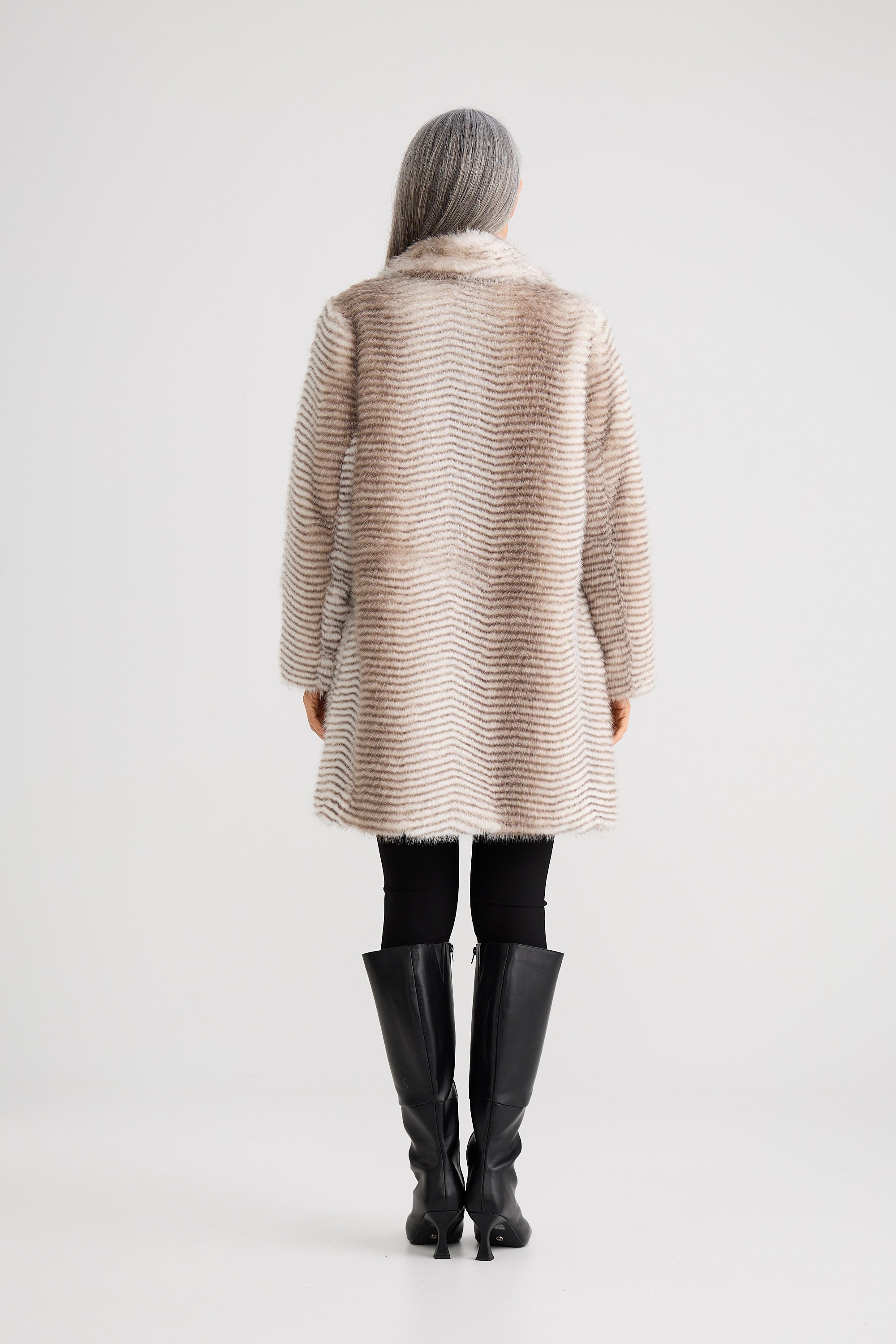 Person wearing a long, light-colored coat with black boots on a white background