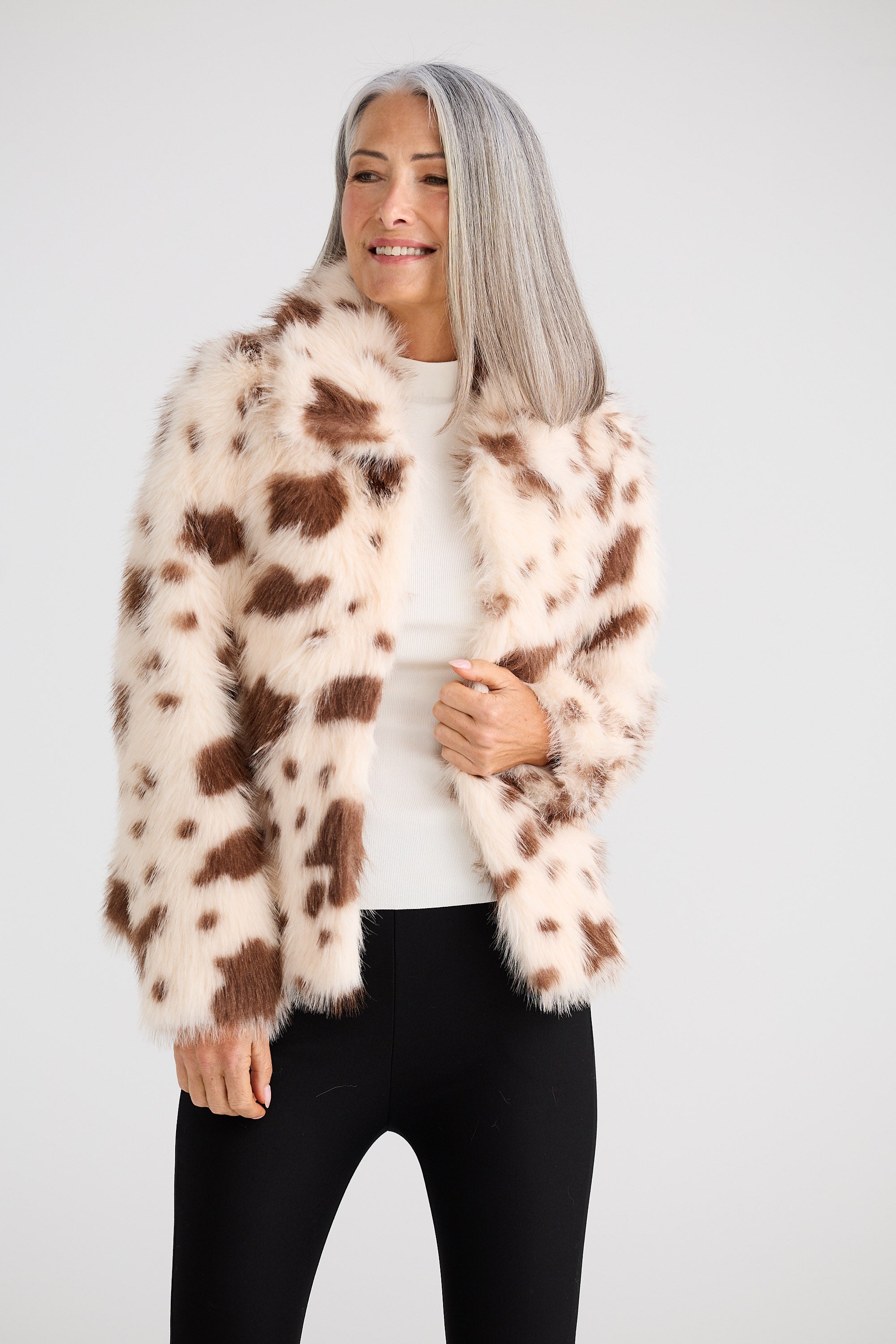 Woman wearing a cow print faux fur jacket on a white background