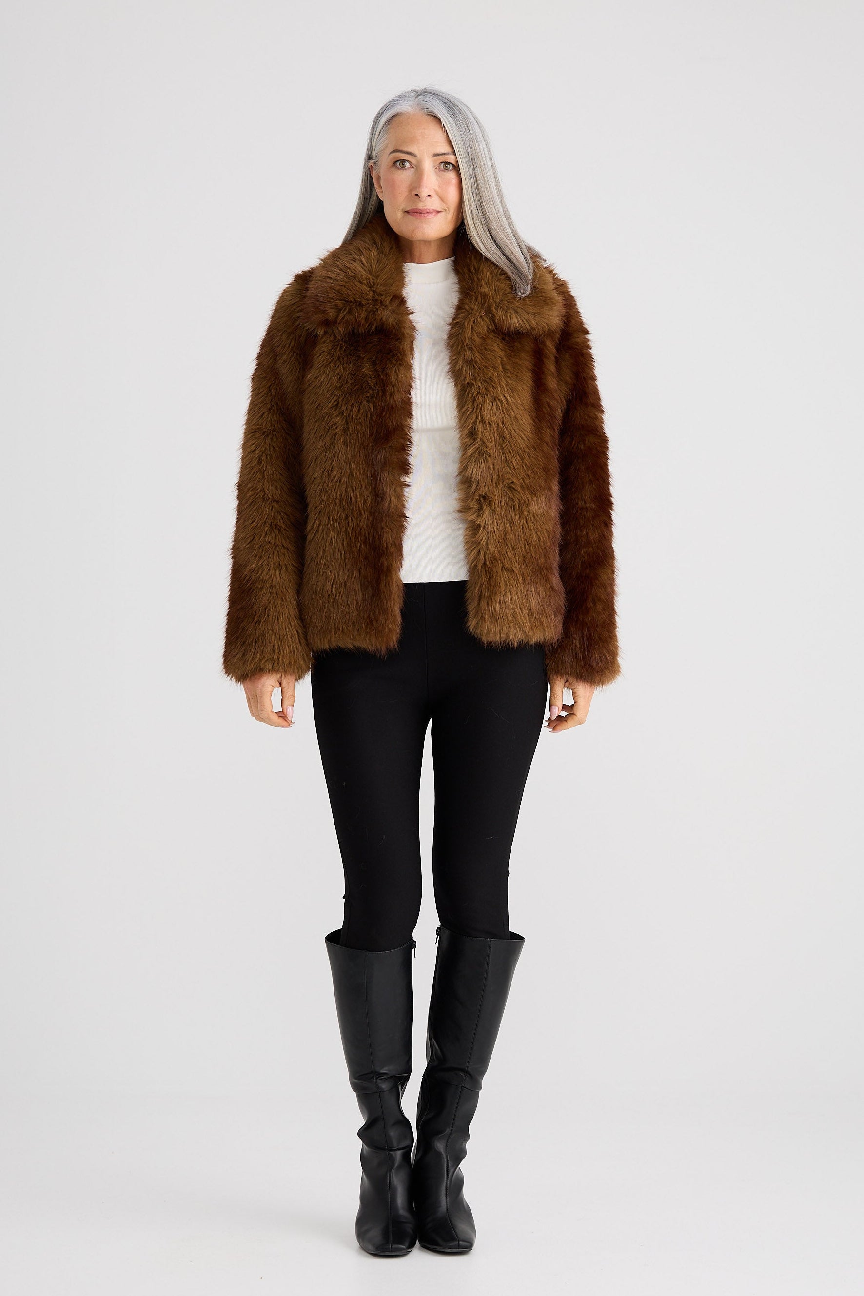 Person wearing a brown faux fur jacket, black leggings, and black boots on a white background