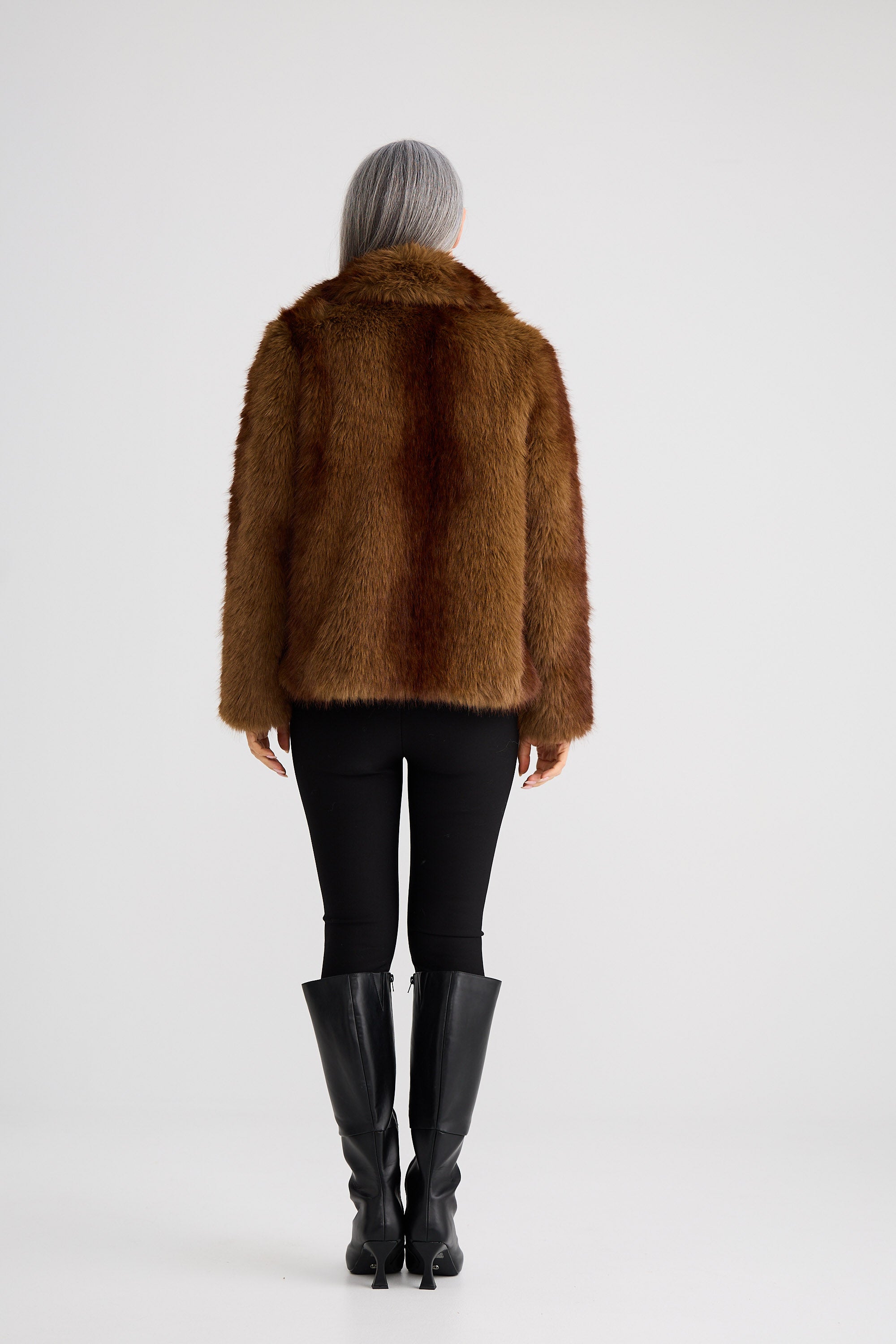 Person wearing a brown fur coat, black leggings, and black boots on a white background