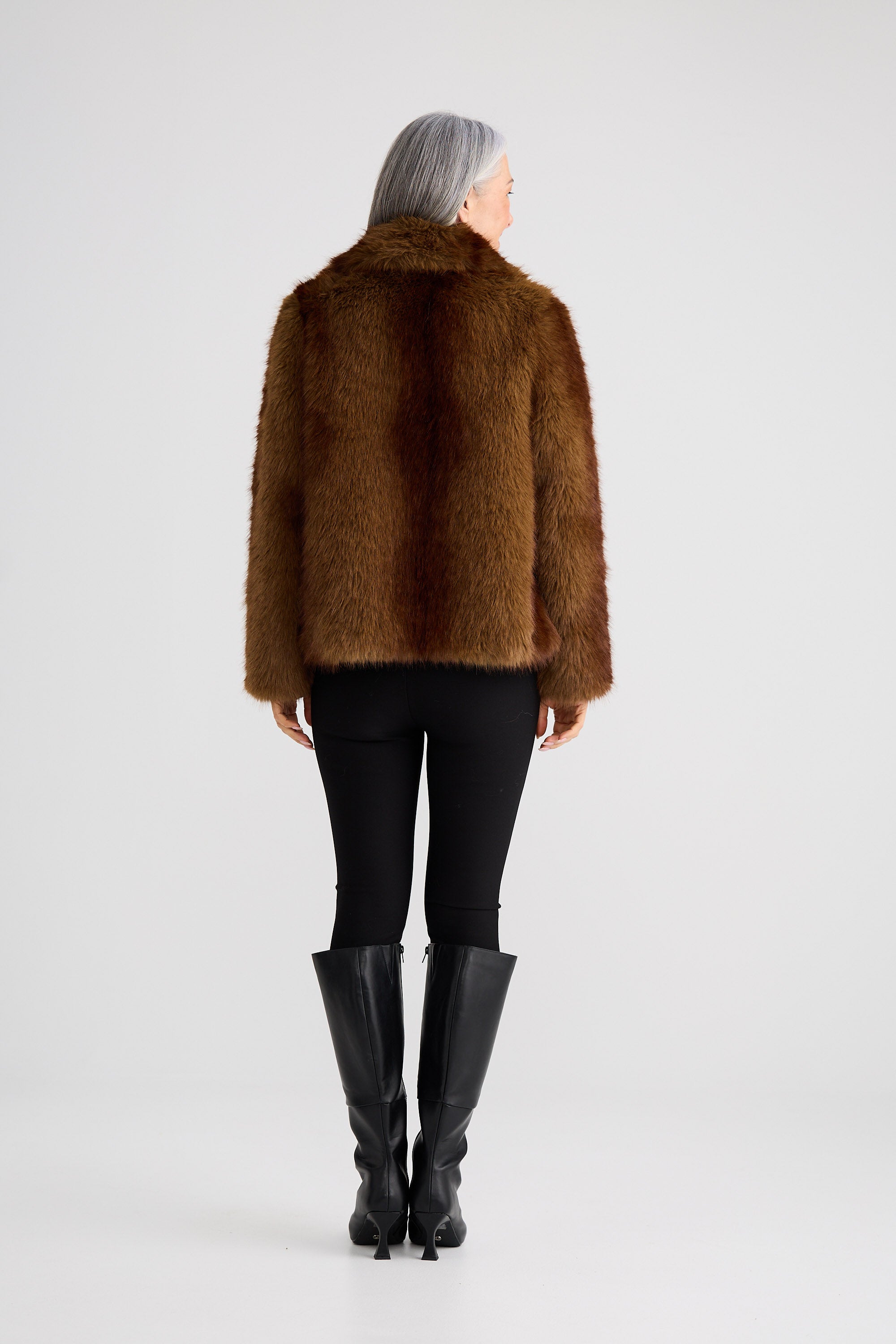 Person wearing a brown fur coat and black pants on a white background