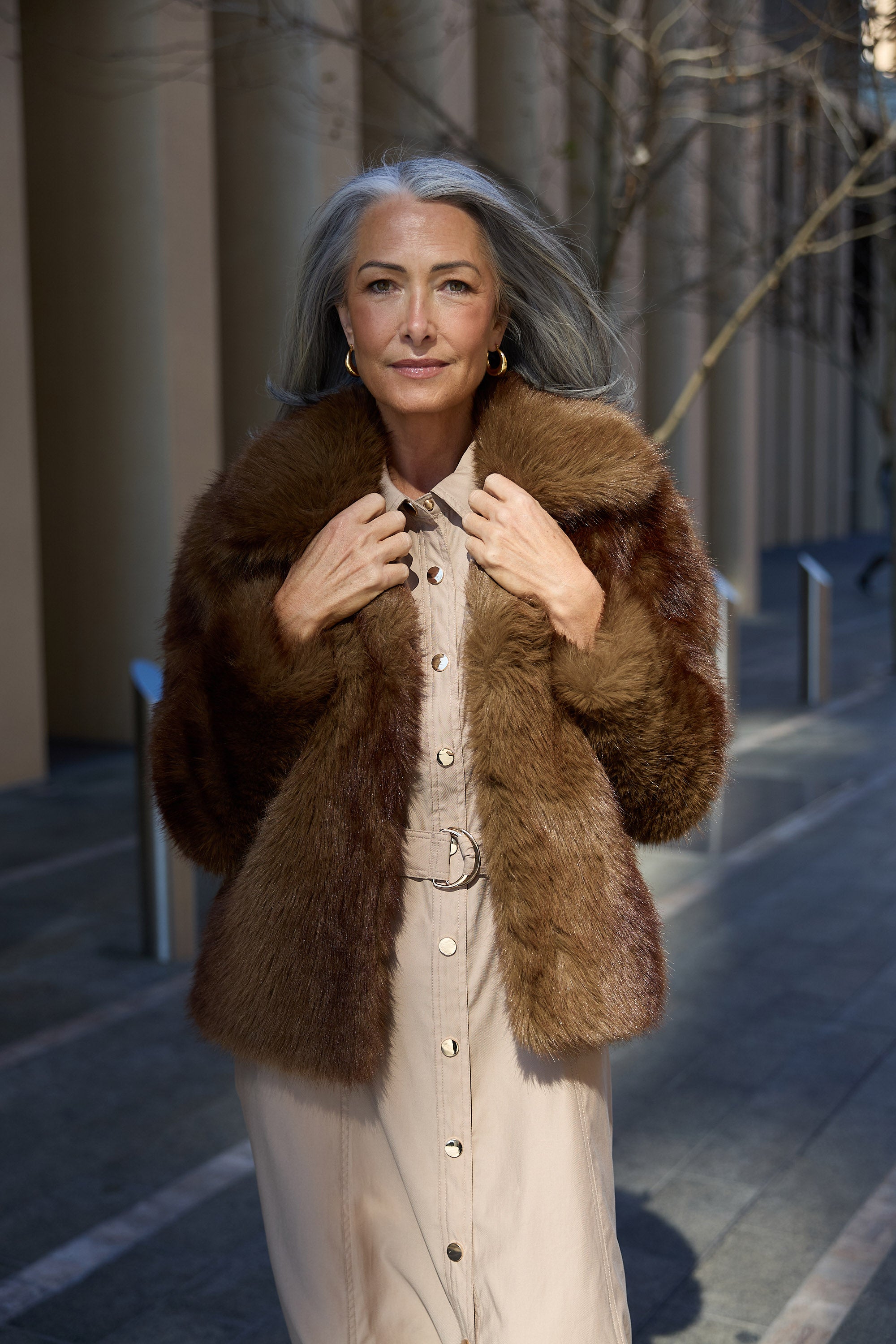 Woman wearing a brown fur coat standing on a city street.