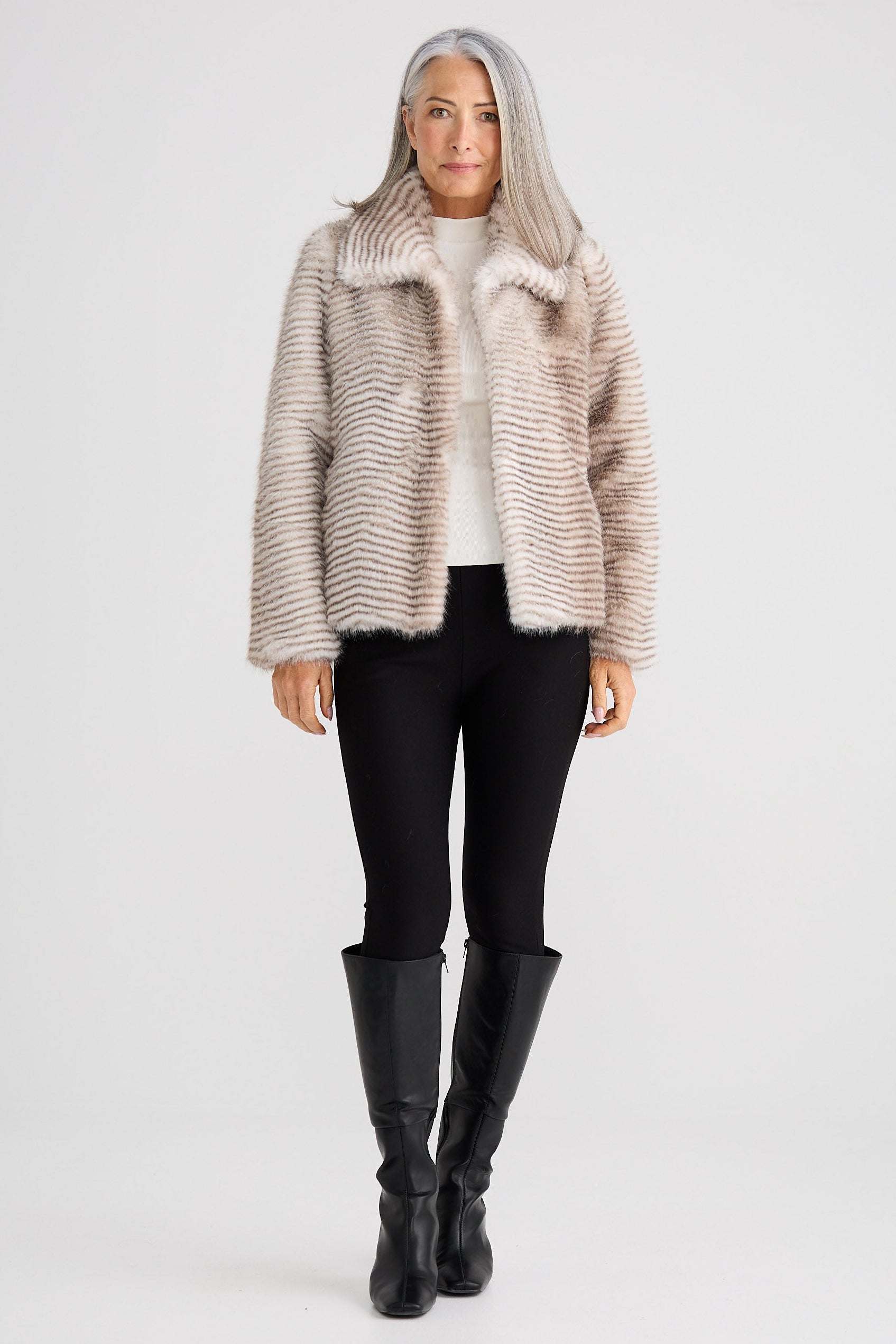 Woman wearing a fur coat, black pants, and black boots on a white background