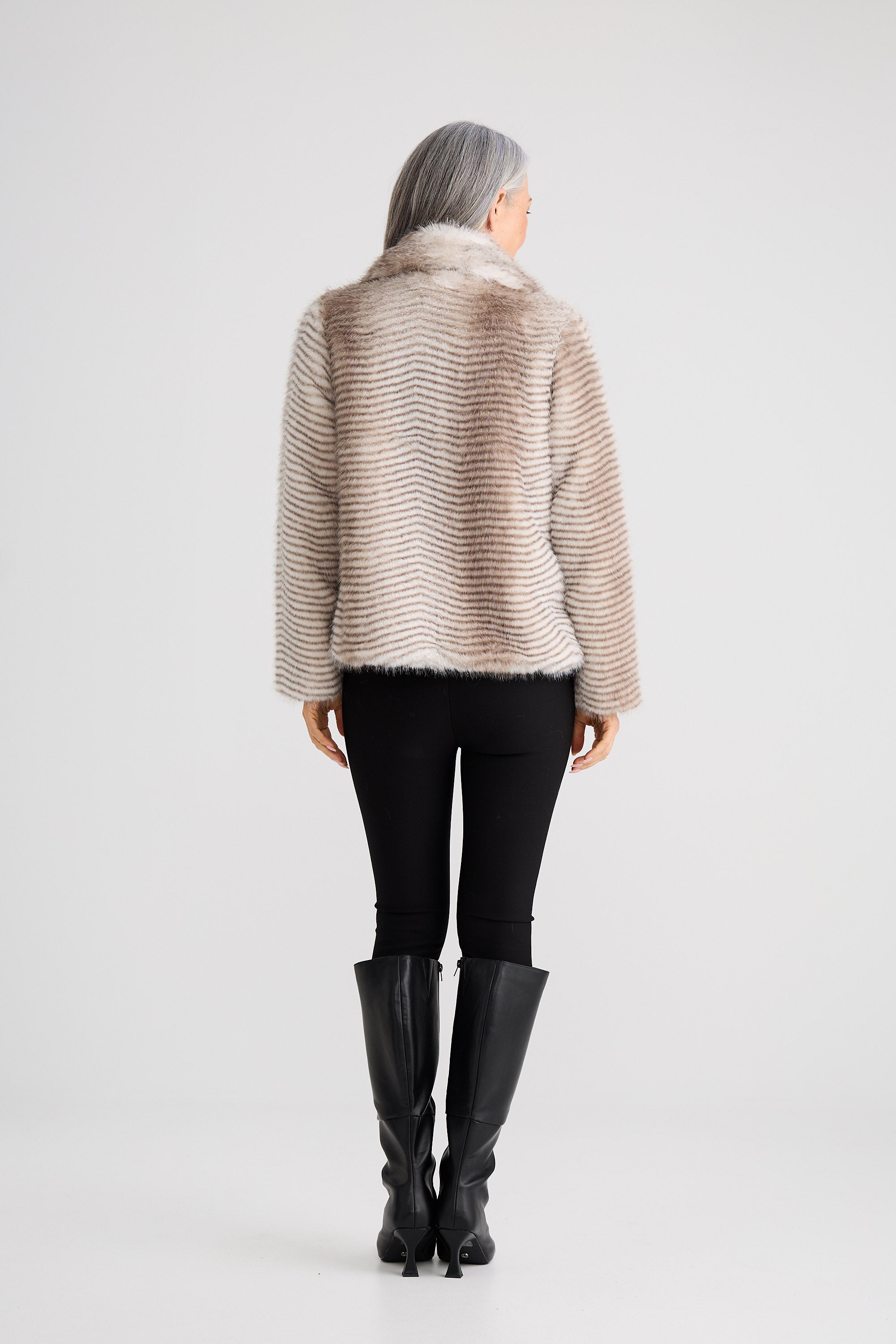 Person wearing a beige knitted sweater and black pants on a white background