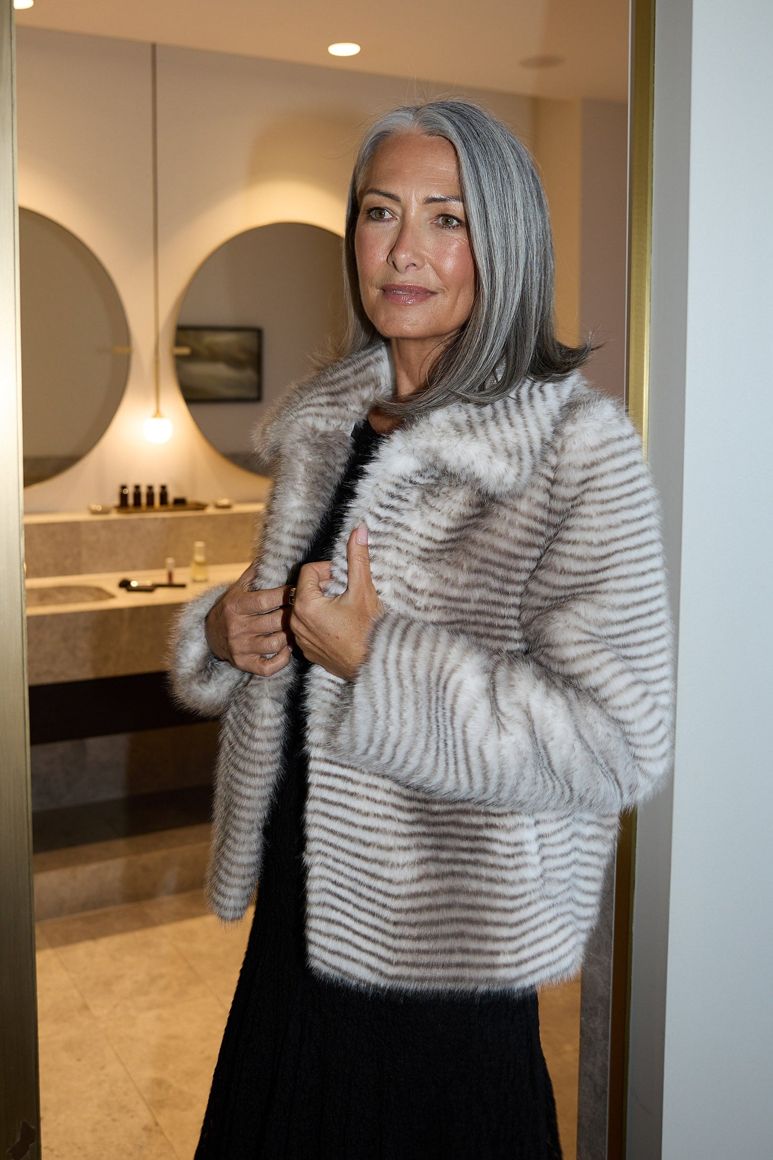 Woman in a fur coat standing in a doorway with a bathroom in the background