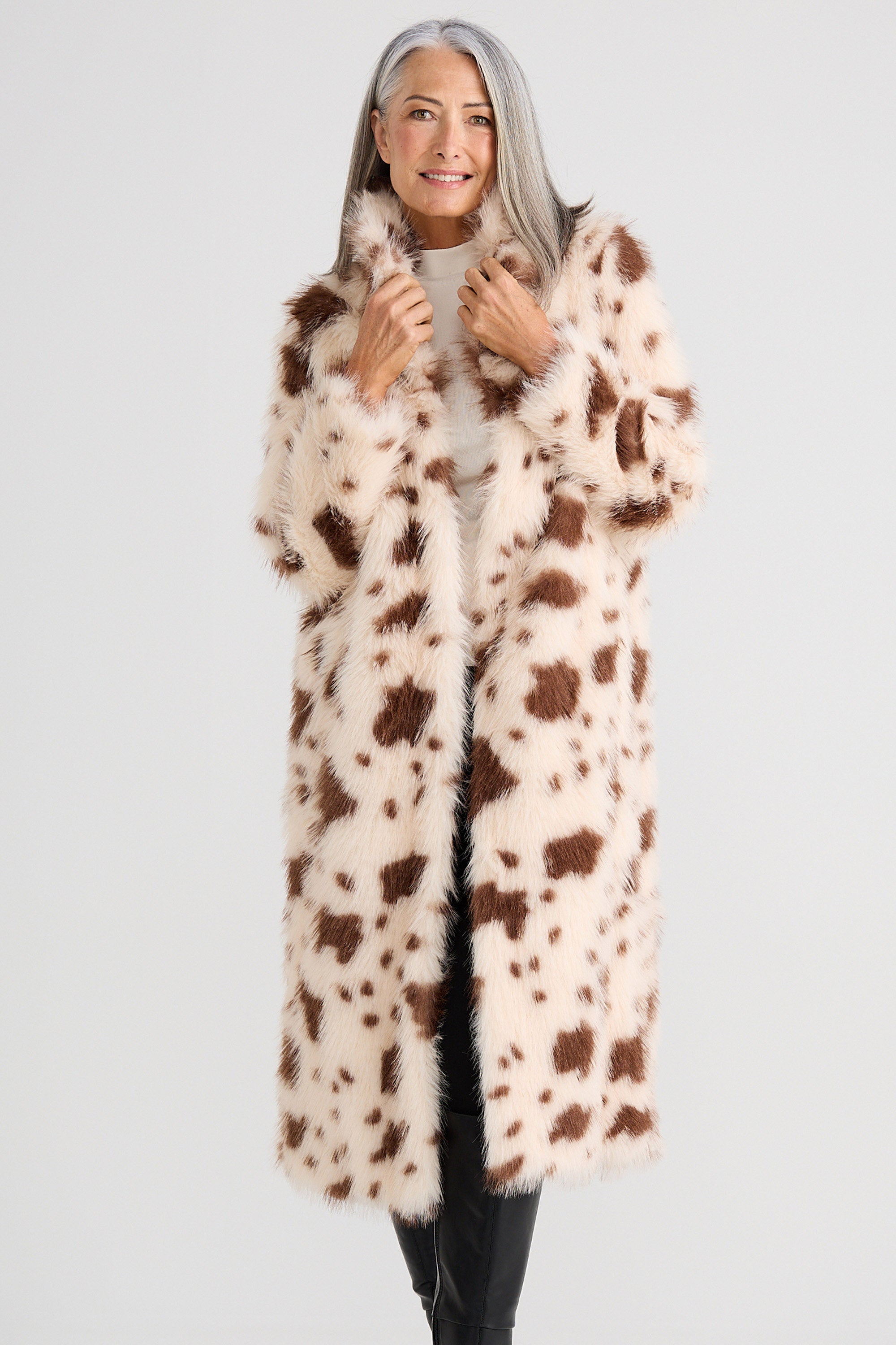 Woman wearing a long, patterned fur coat against a plain background