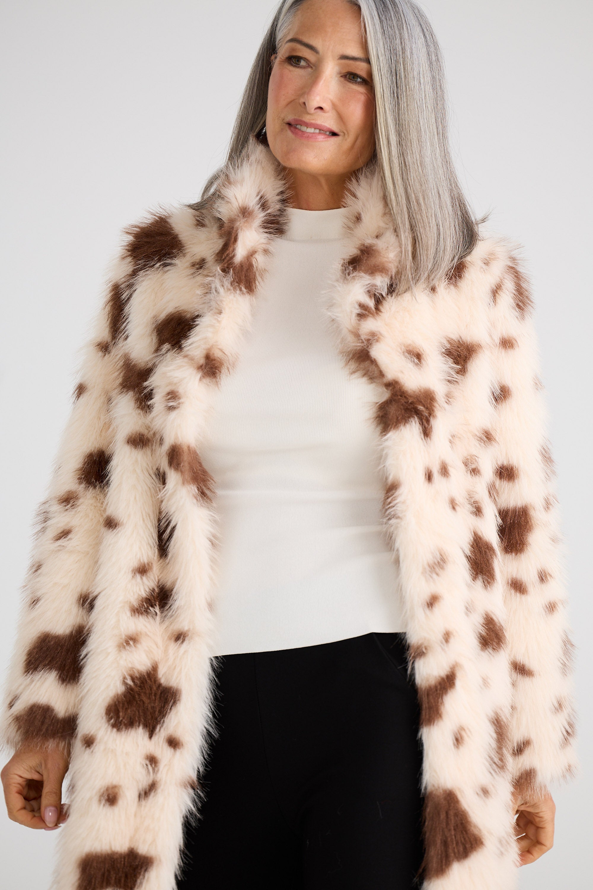 Woman wearing a cow print fur coat against a white background