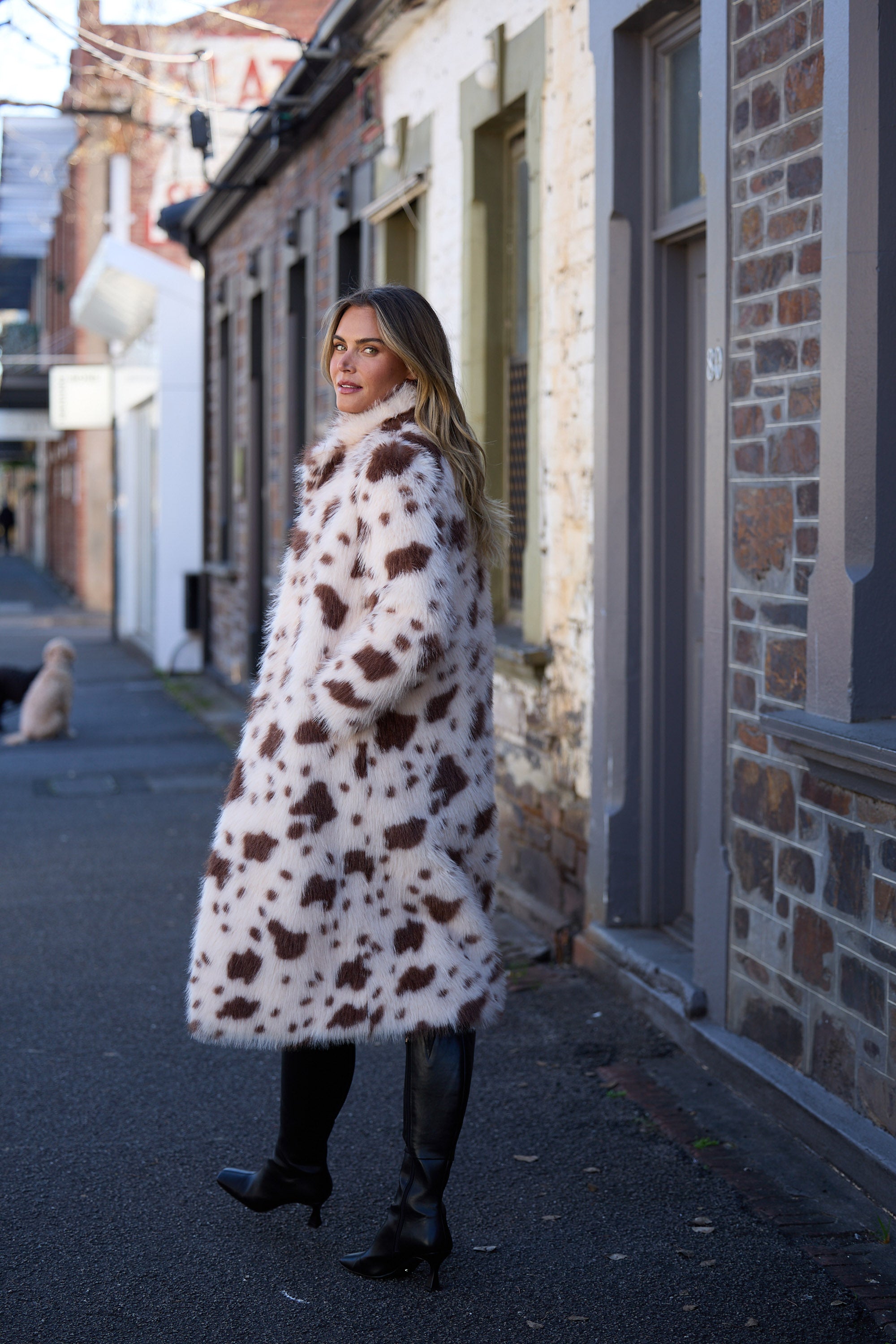 Woman wearing a cow print coat standing on a street.