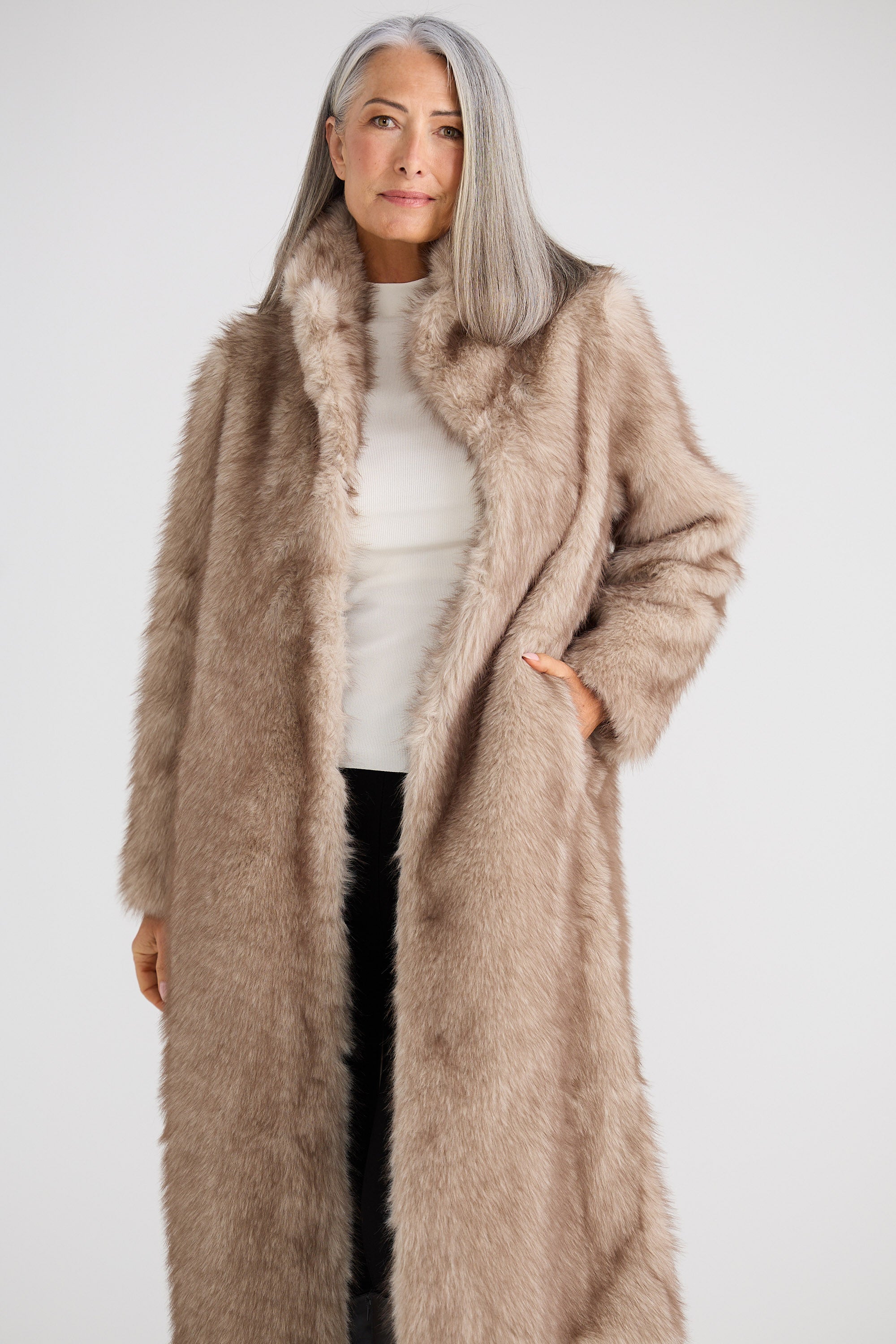 Woman wearing a long beige fur coat against a white background