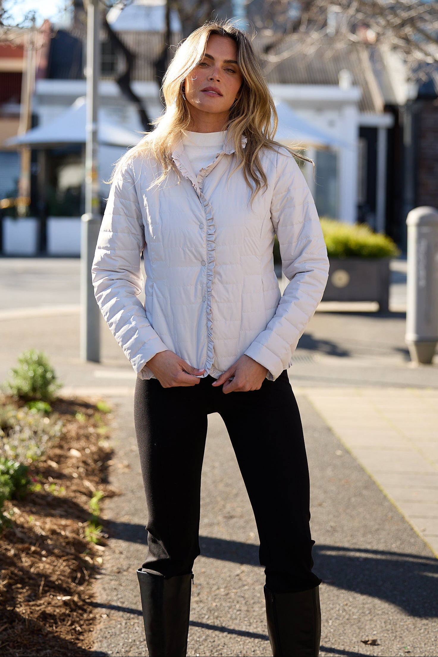 Woman standing on a sidewalk wearing a light-colored shirt and dark pants.
