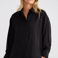 Woman wearing a black shirt and beige pants against a white background