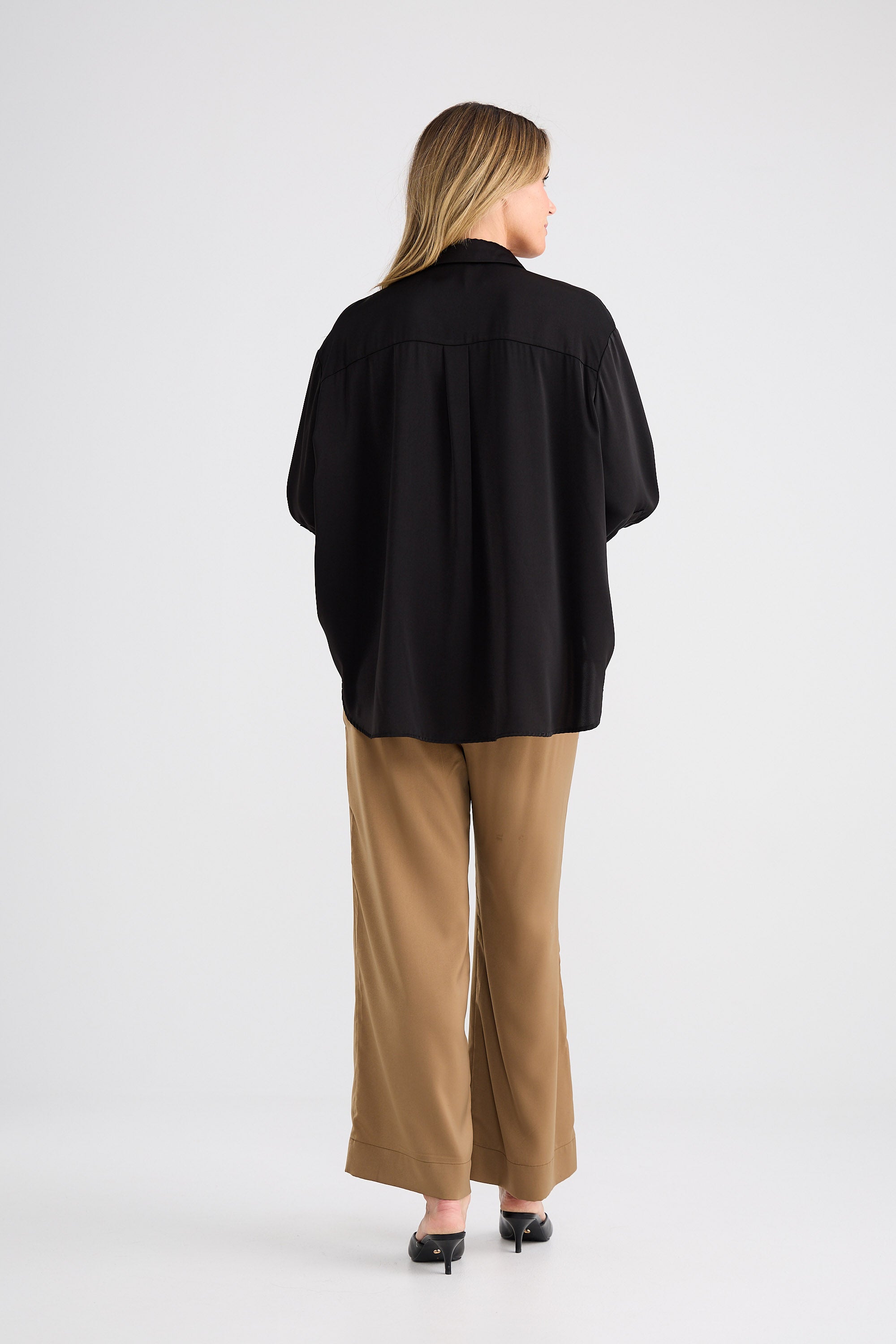 Person wearing a black shirt and beige pants on a white background