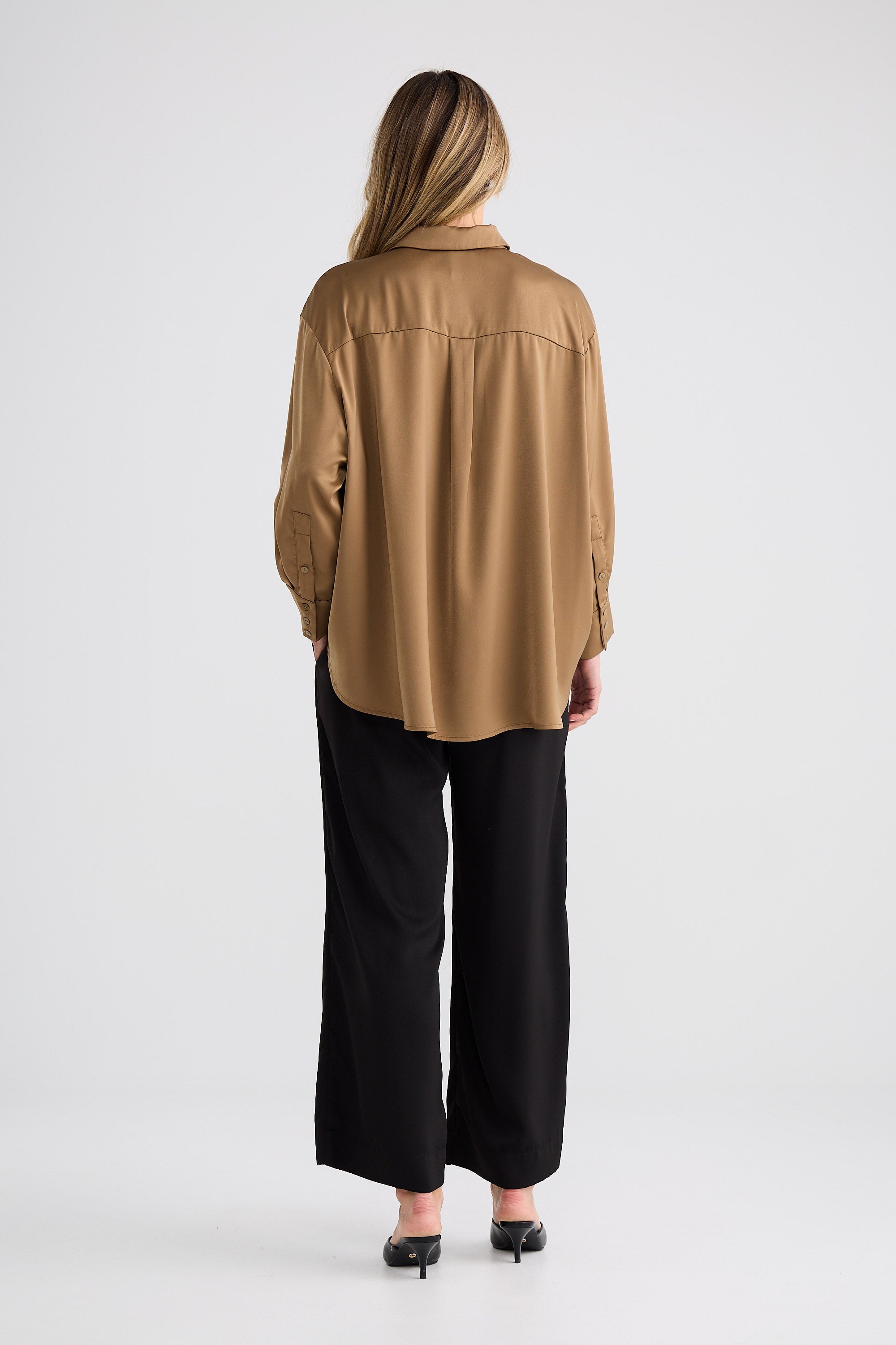 Person wearing a tan blouse and black pants on a white background