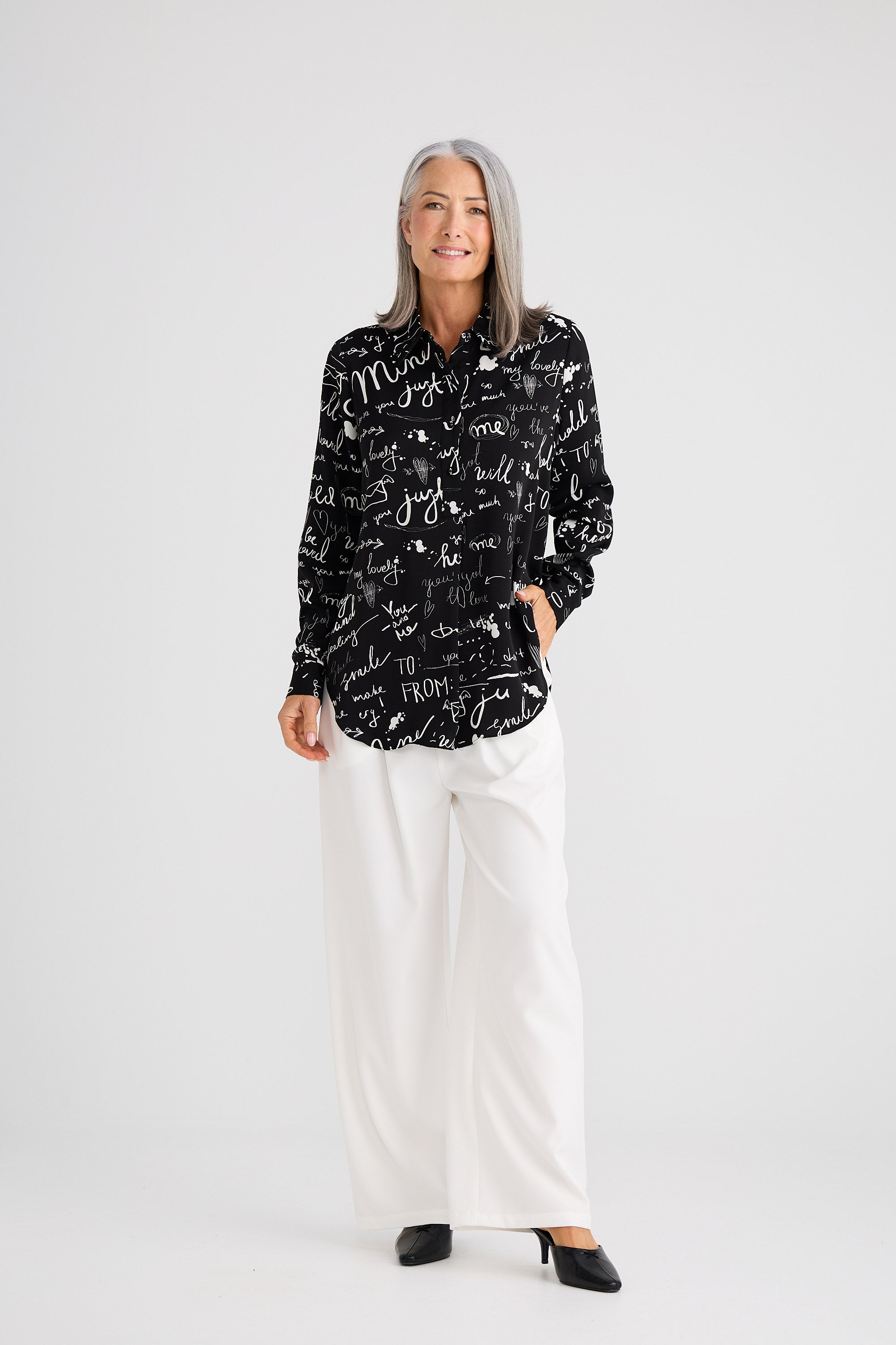 Woman wearing a black patterned shirt and white pants on a white background