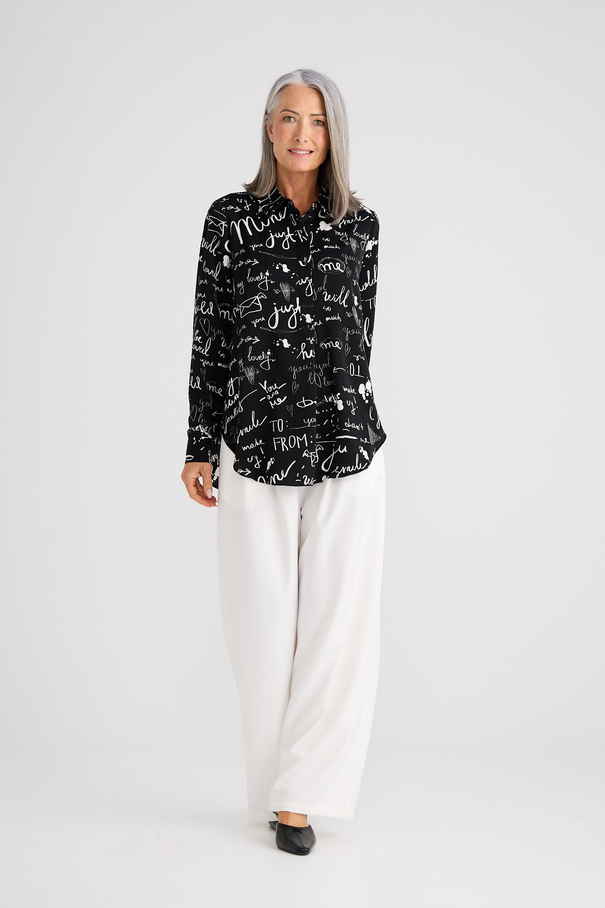 Woman wearing a black patterned shirt and white pants on a white background