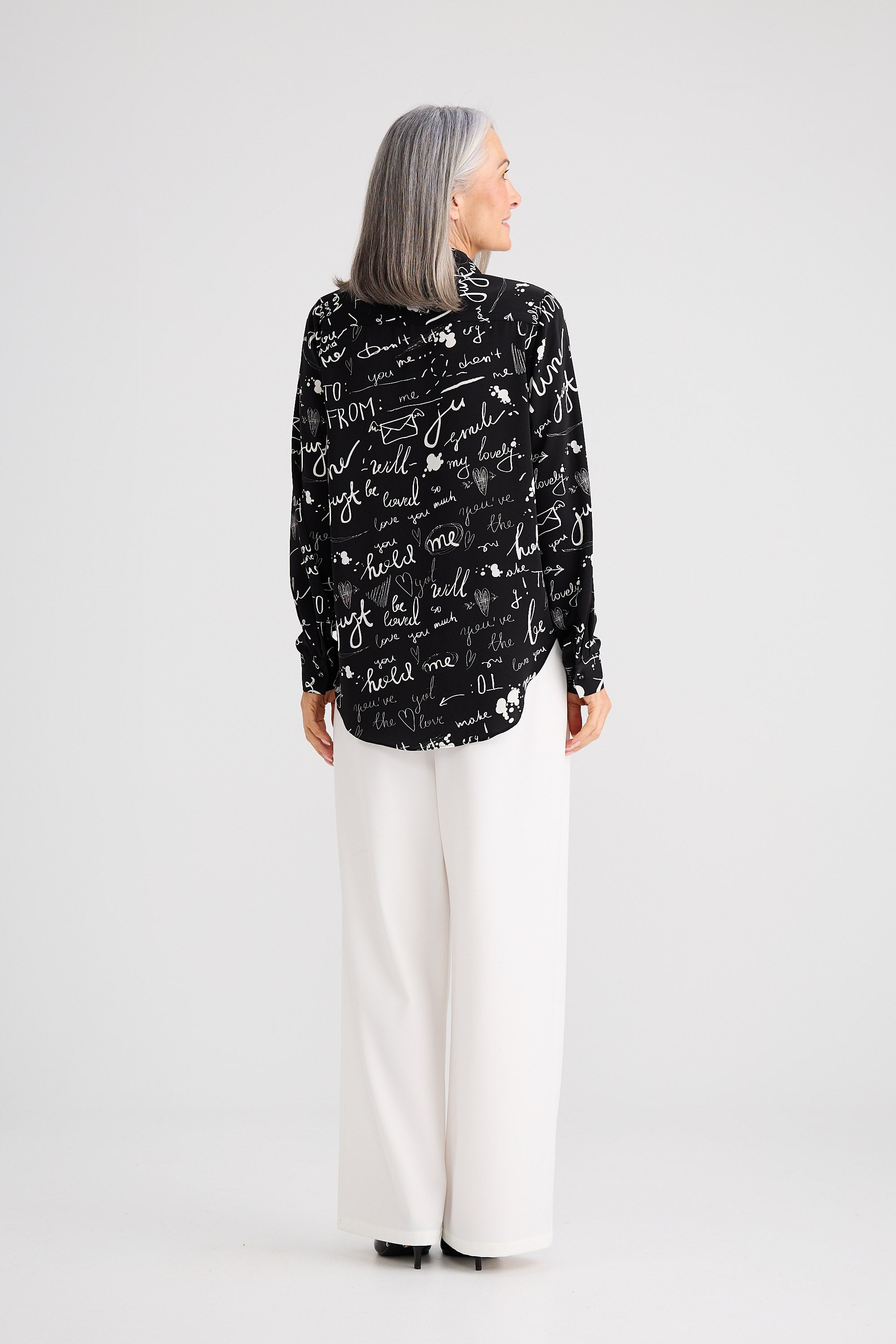 Person wearing a black patterned jacket and white pants on a white background