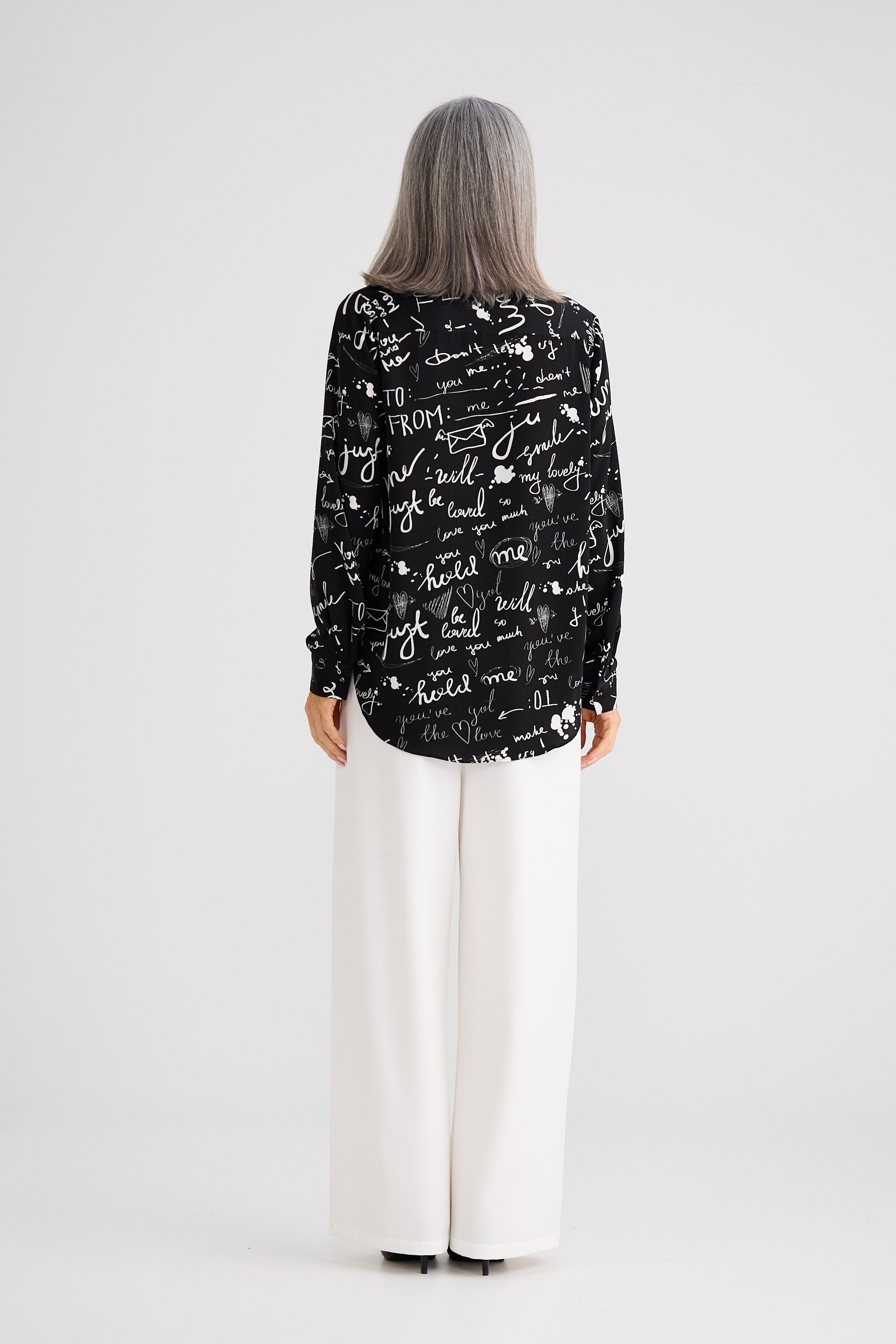 Person wearing a black patterned shirt and white pants on a white background