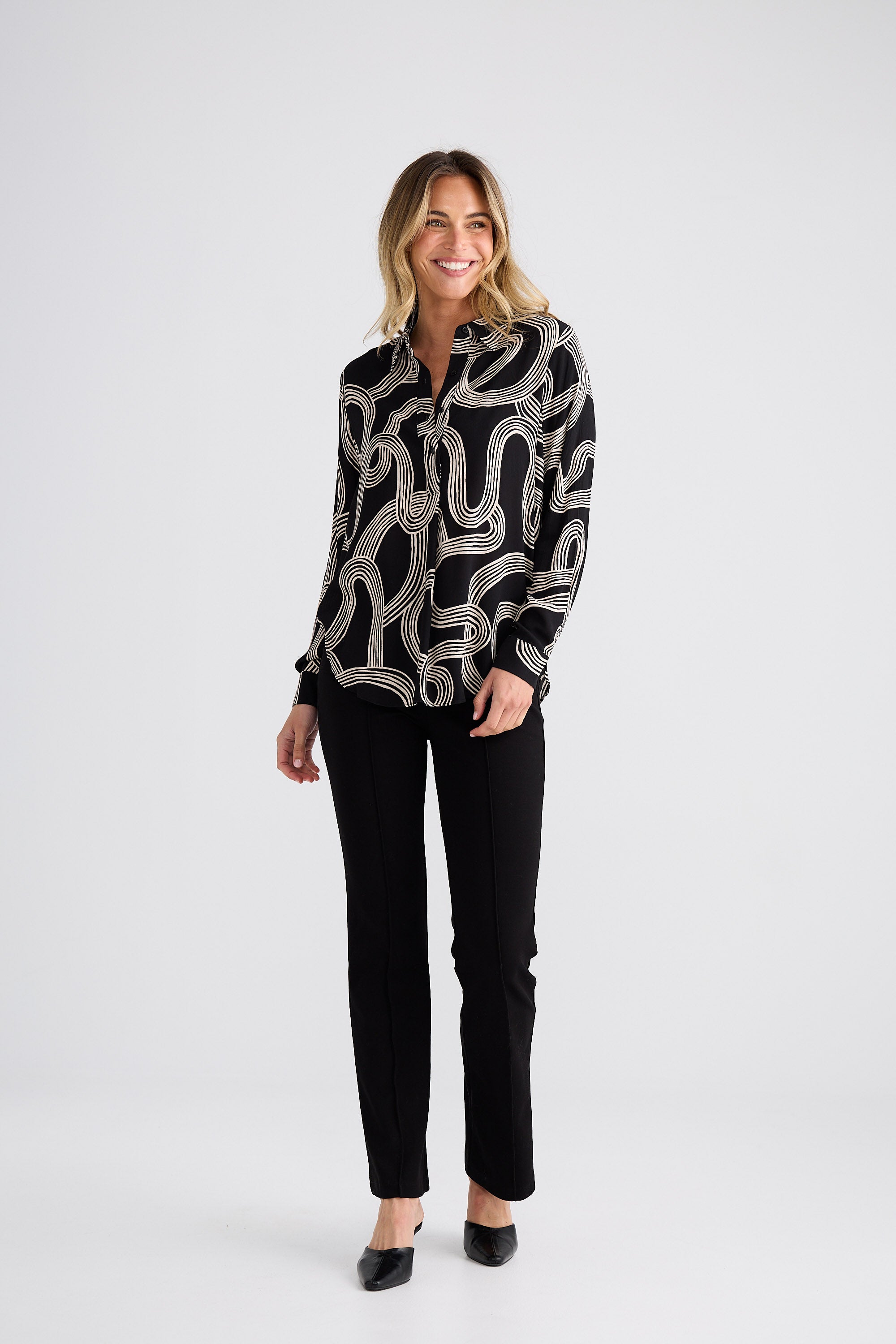 Woman wearing a black and white patterned blouse with black pants on a white background